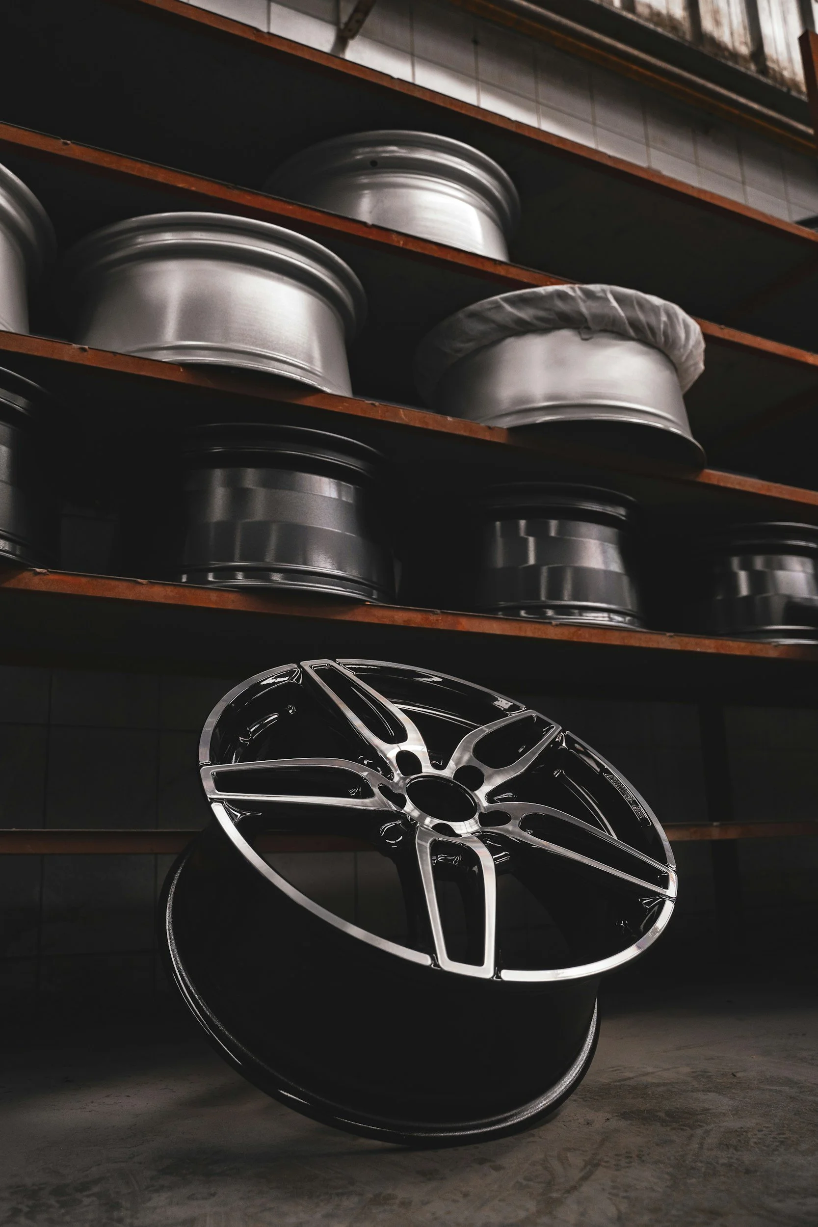 Stacked automotive wheels on shelves and a shiny alloy wheel in the foreground.