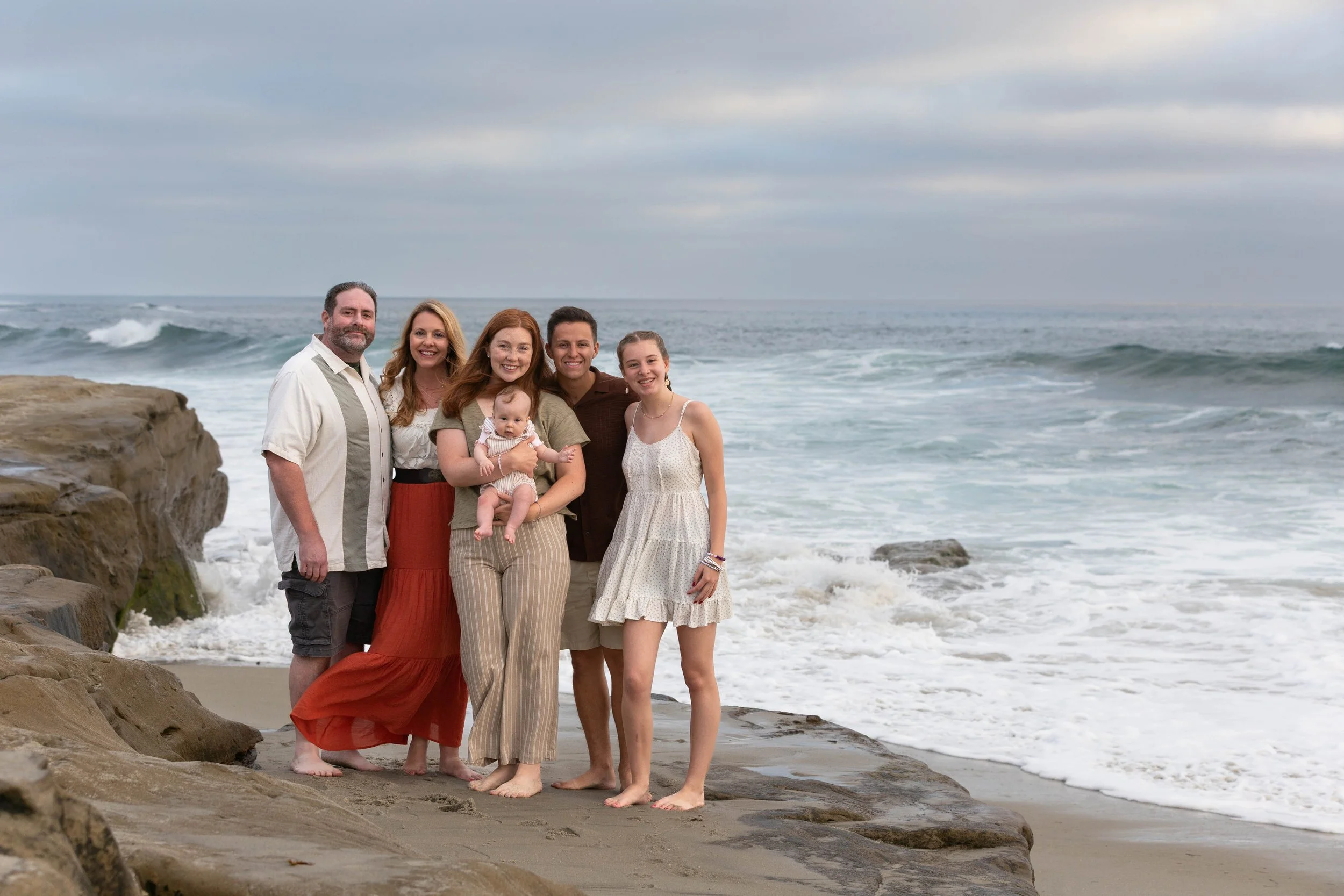 Family posing with a baby on rocky coastal cliffs beside ocean waves