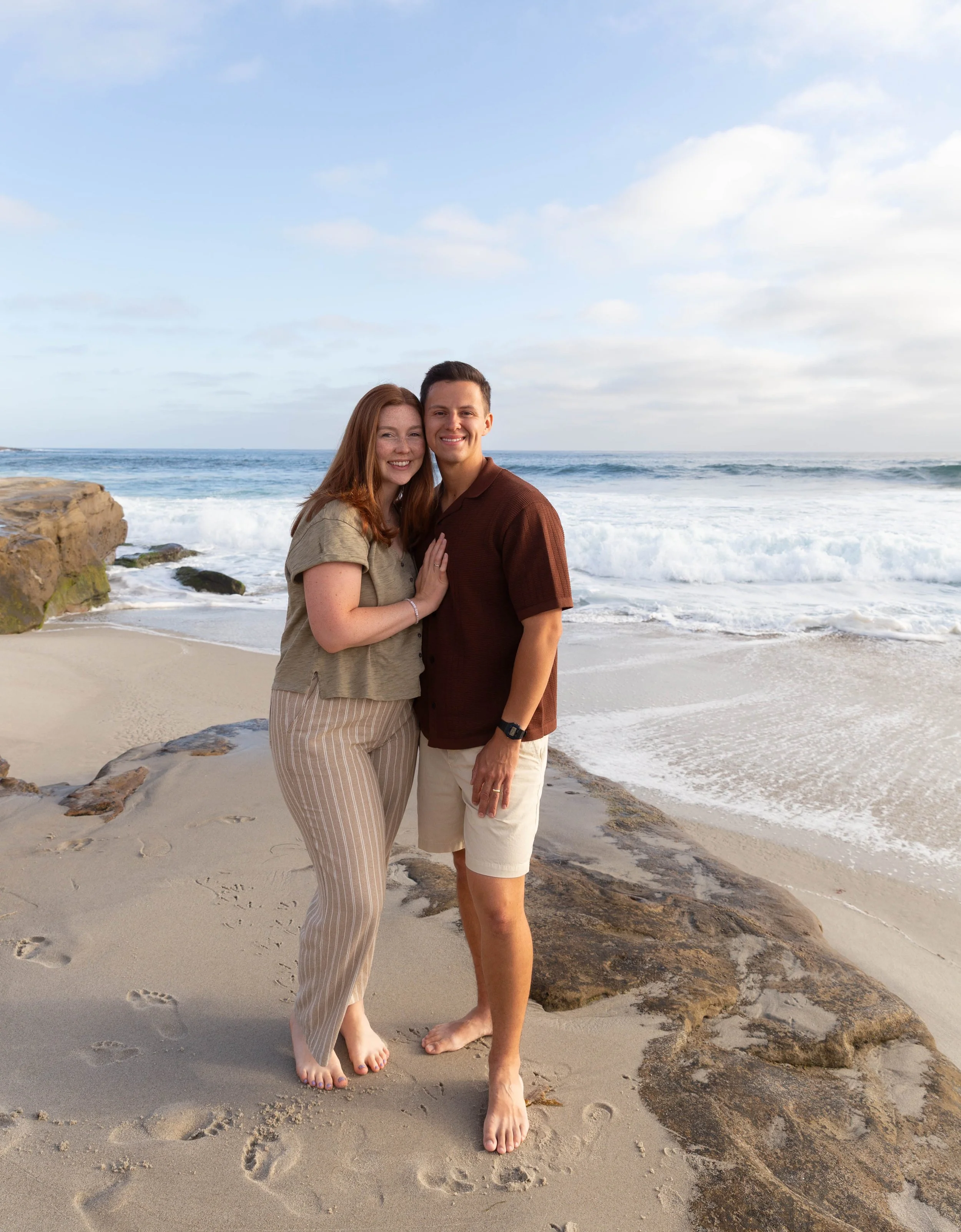 Happy couple embracing on a sandy beach beside ocean waves and rocky shoreline