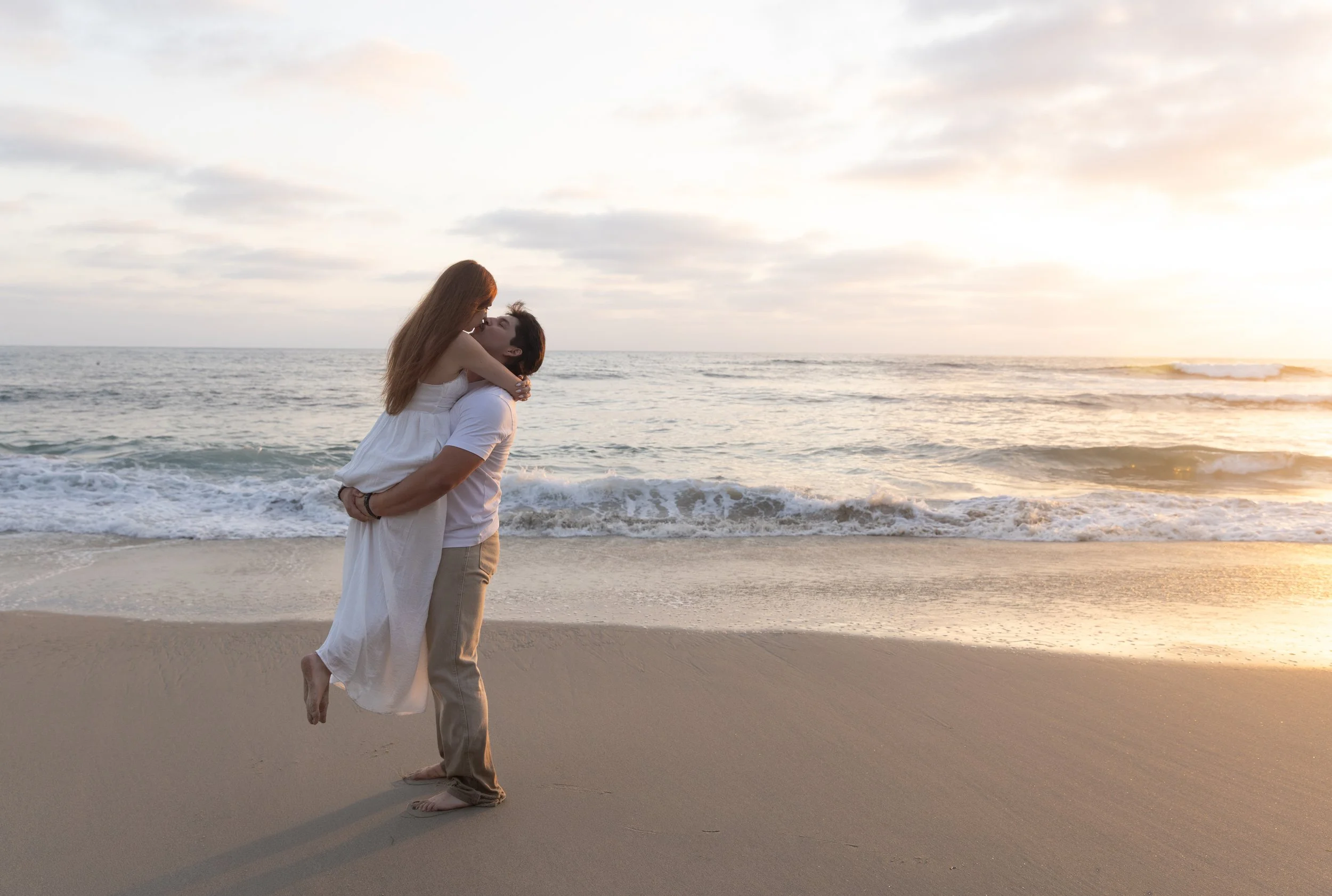 Couple embracing and kissing on a sandy beach at sunset