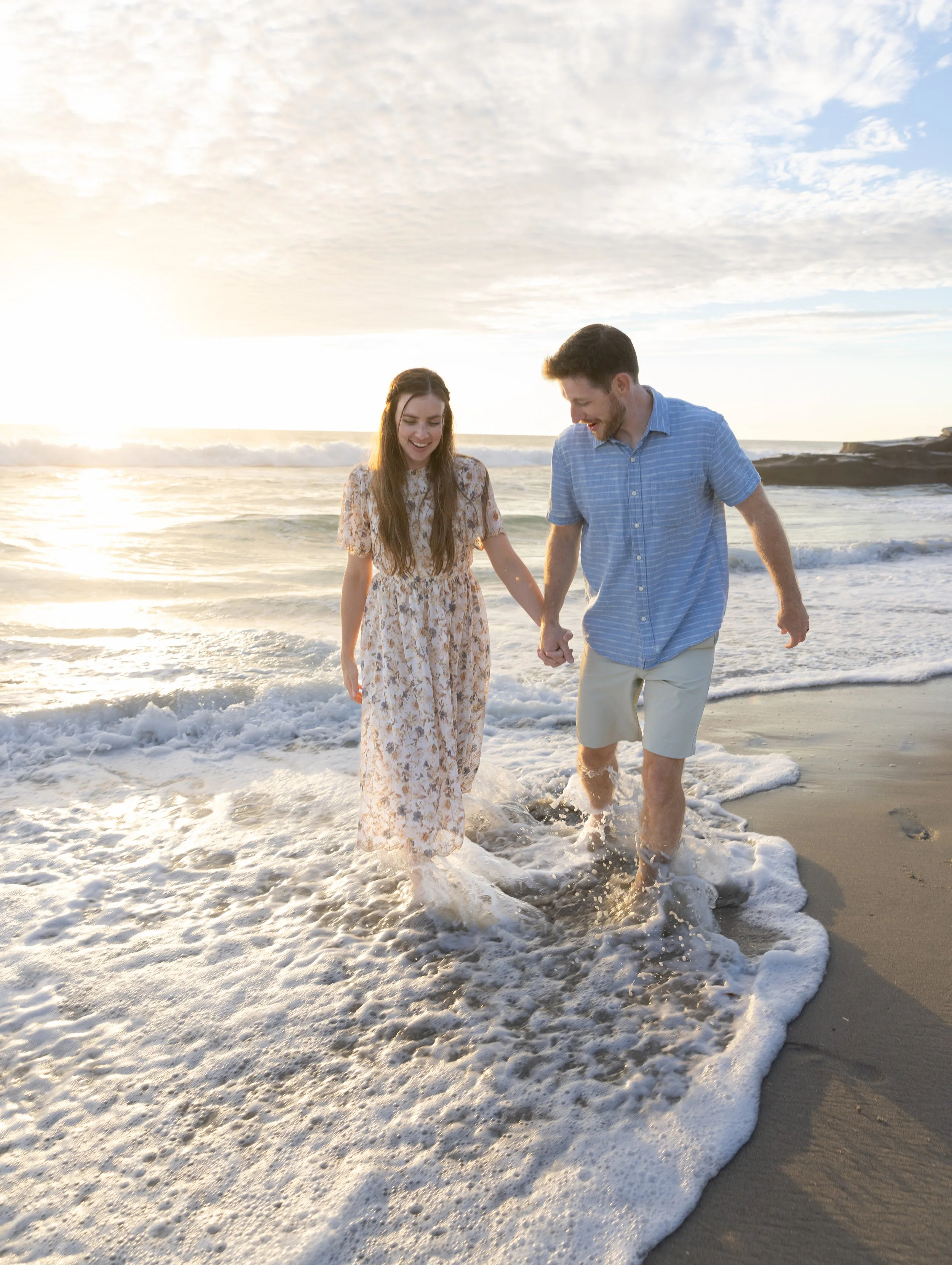 Smiling couple holding hands while walking along a sunlit beach in the ocean surf