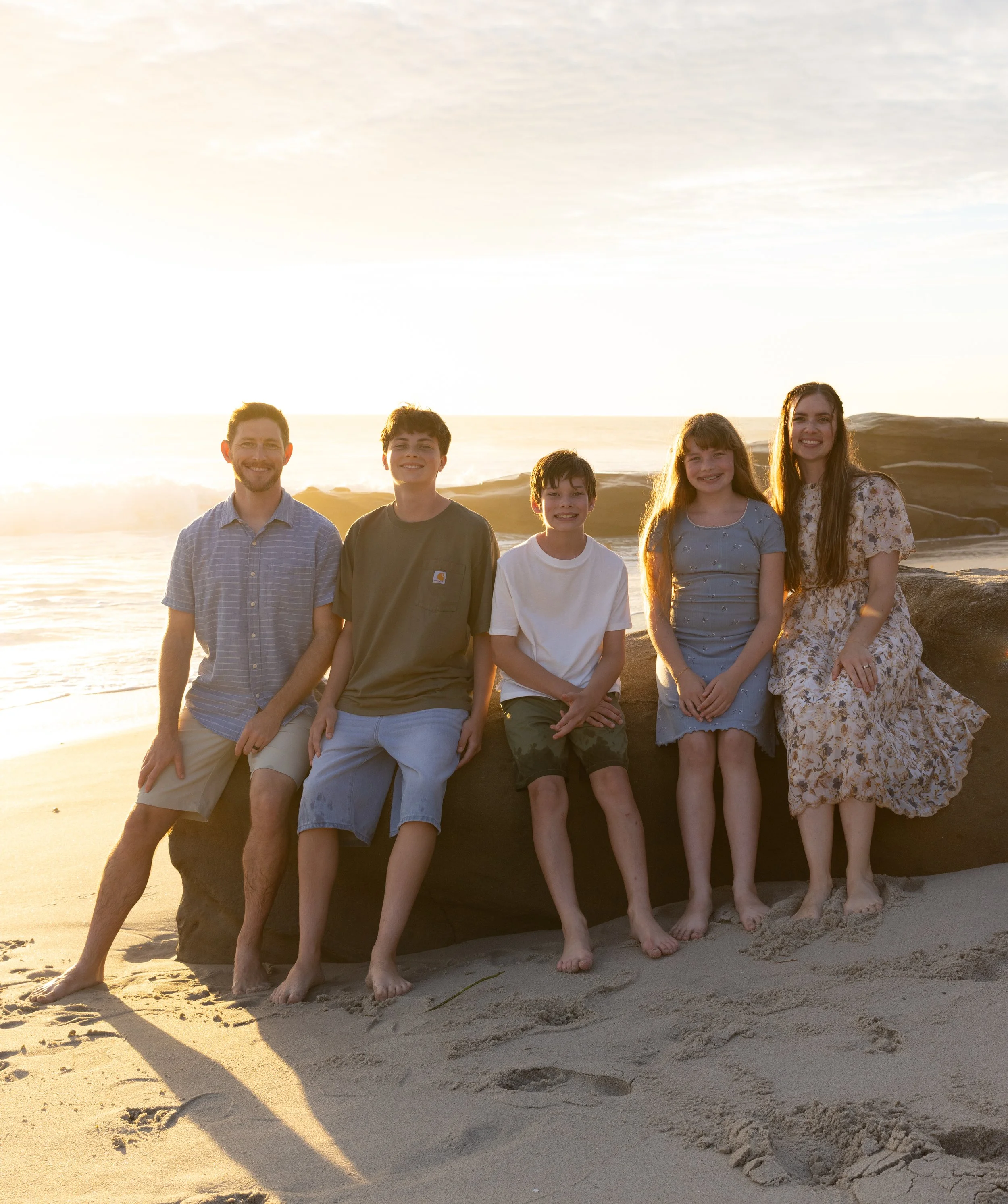Family of five posing on a beach rock at sunset
