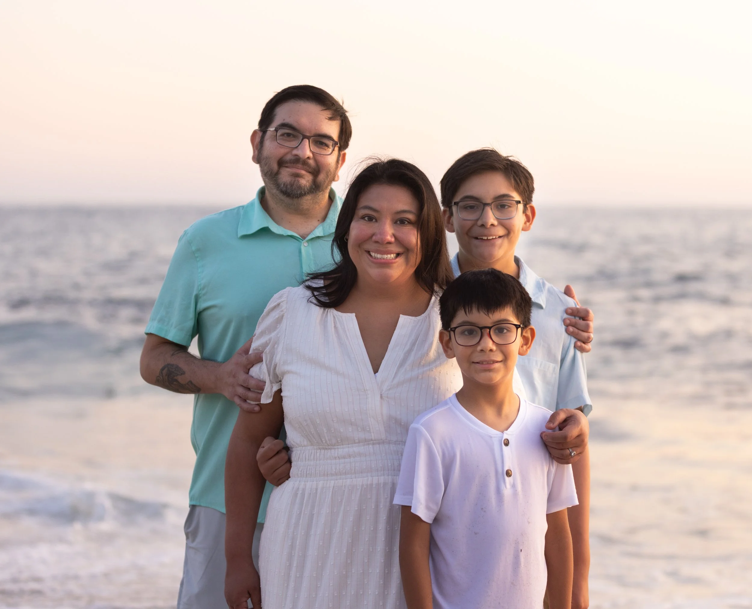 Smiling family of four posing together on a beach at sunset