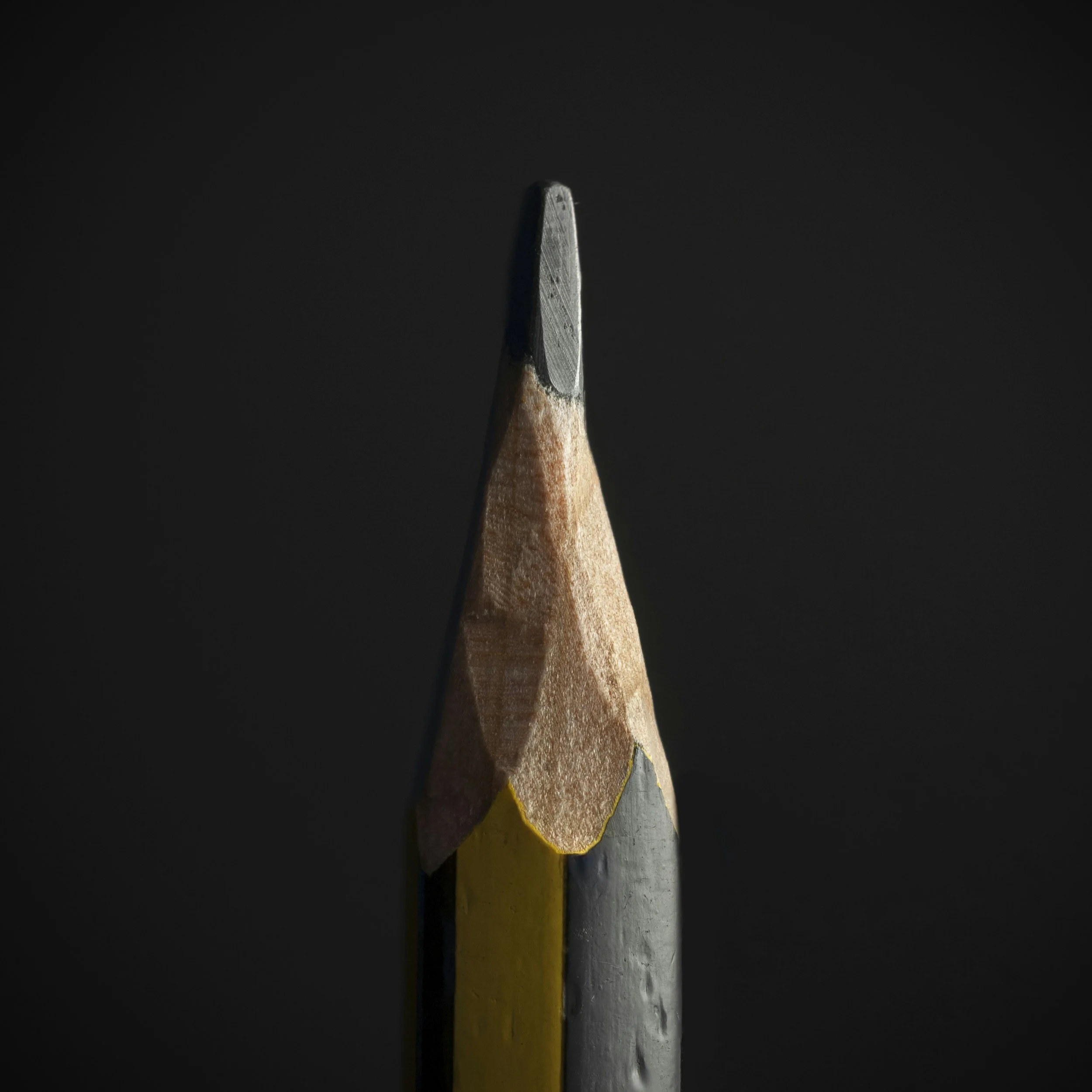 Close-up of the tips of six differently colored pencils arranged vertically against a black background.