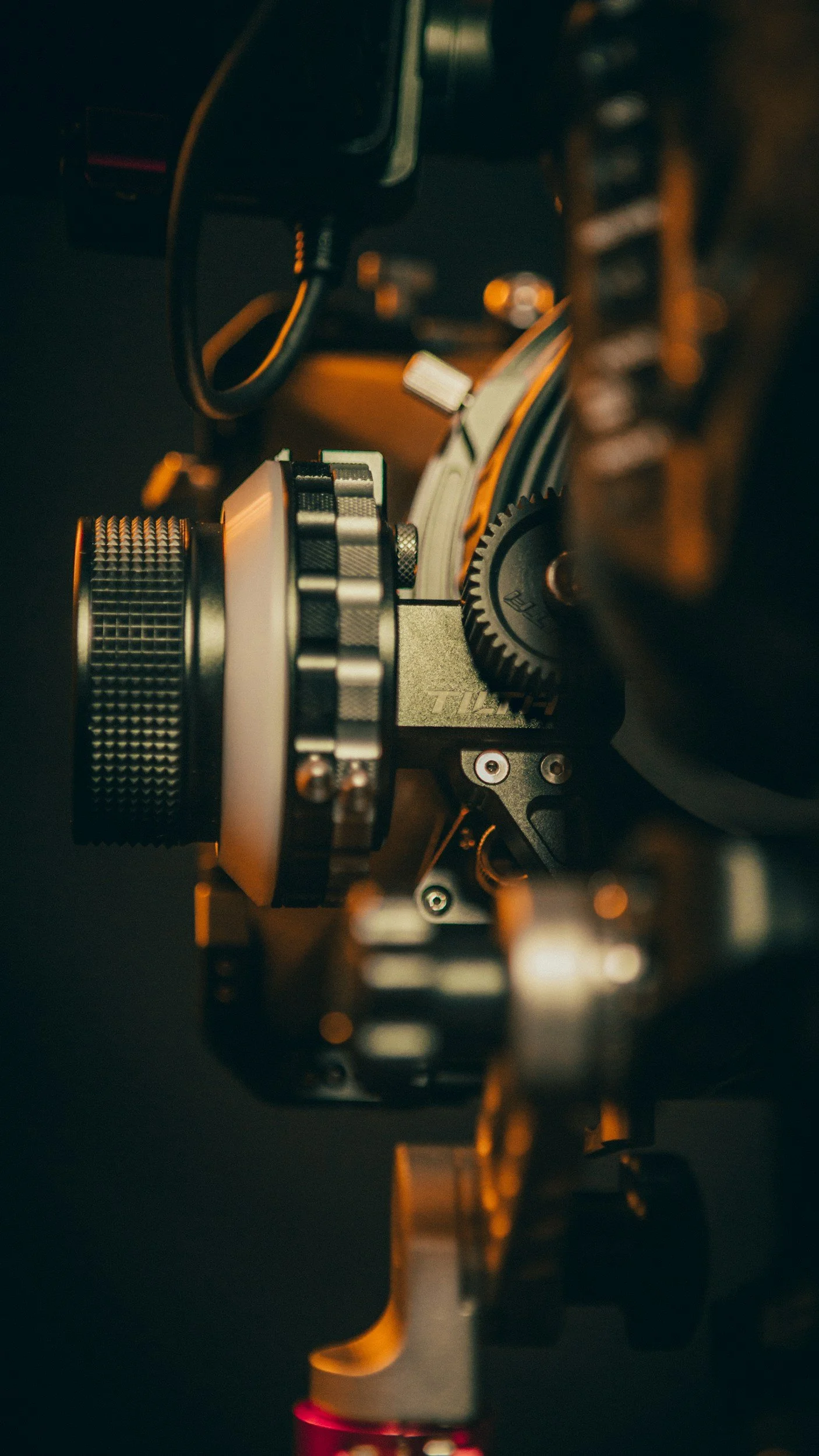 Close-up of a camera rig with various mechanical and electronic components, including gears and screws, illuminated with warm, ambient lighting.