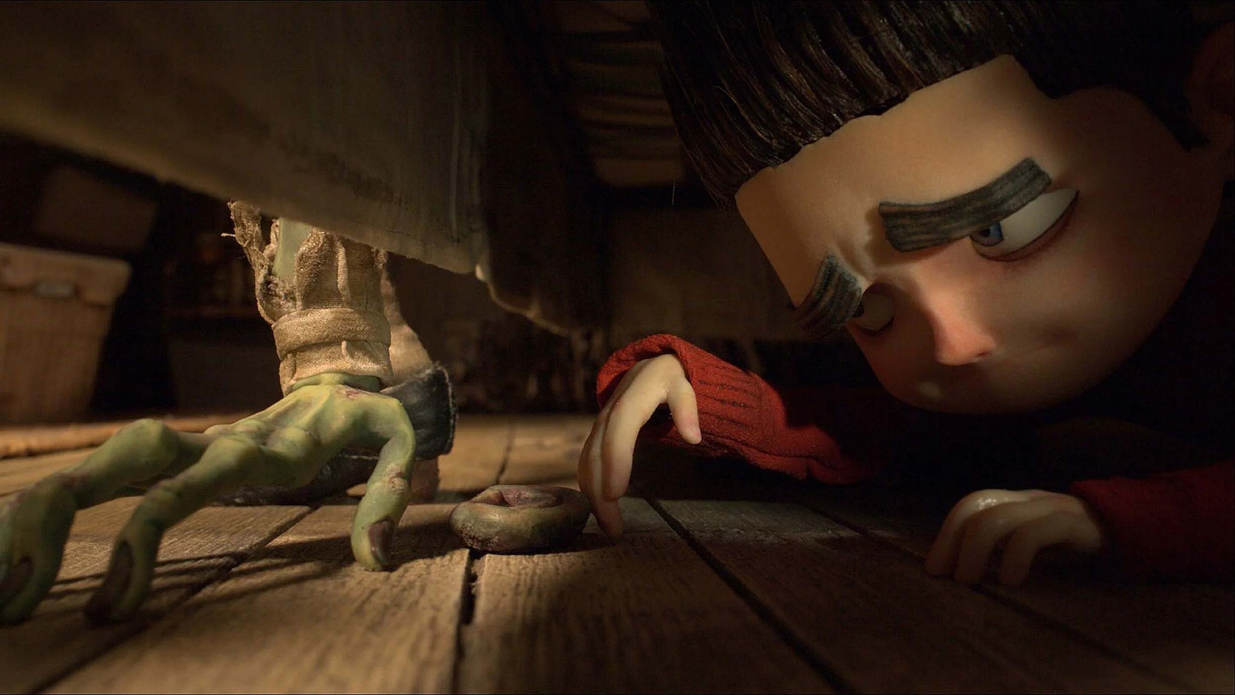 A puppet boy with dark hair, wearing a red shirt, is lying on the wooden floor, looking towards a green, slimy creature with multiple limbs that is crawling on the floor.
