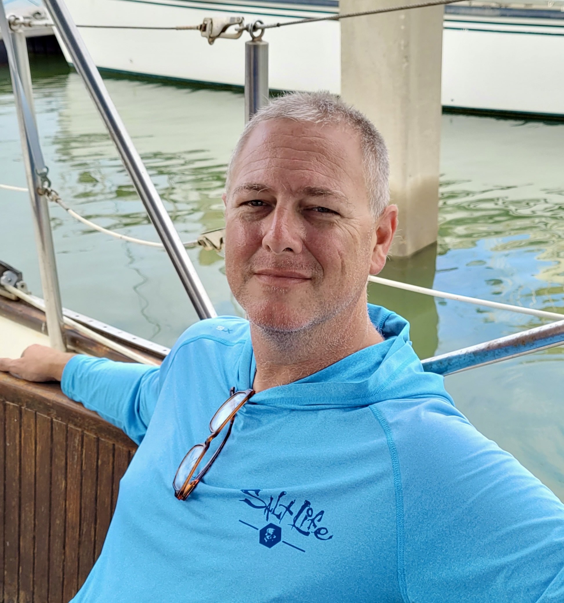 Close-up of a retired fire fighter with short gray hair smiling on a boat, with water, railing, and boat structure in the background.