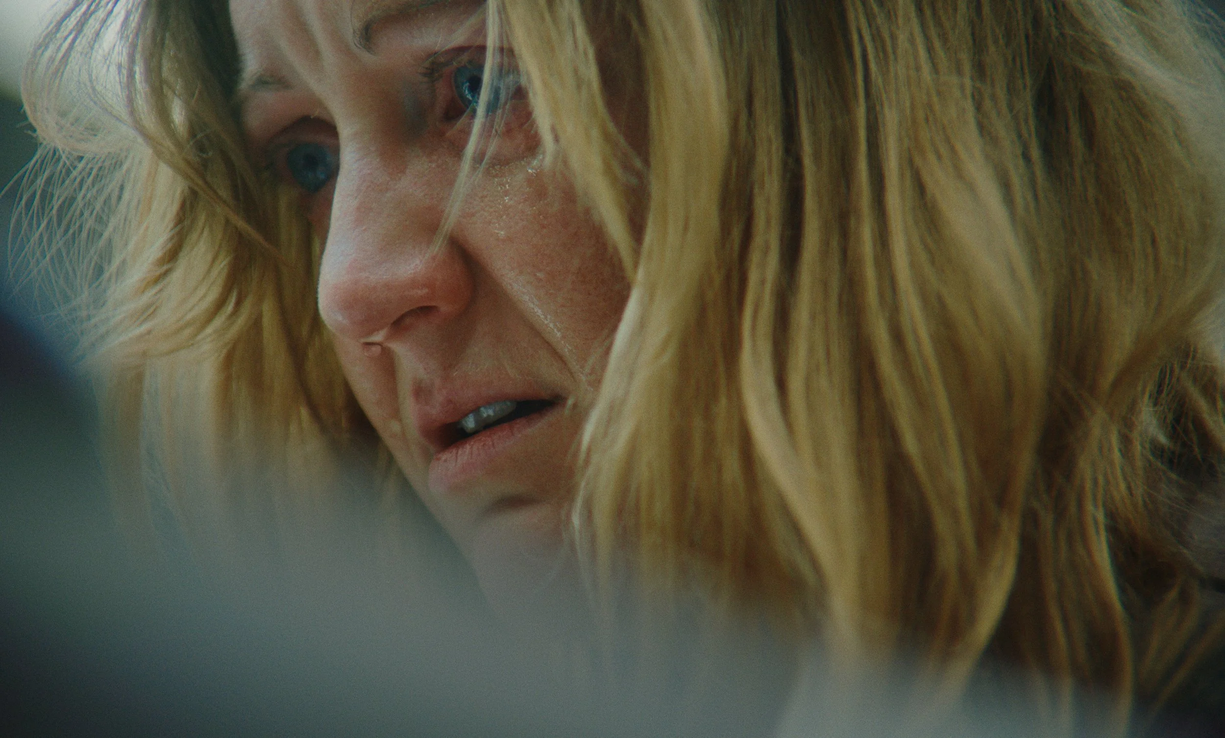 Close-up of a woman with blonde hair and blue eyes, looking intently downward, with a focused expression.