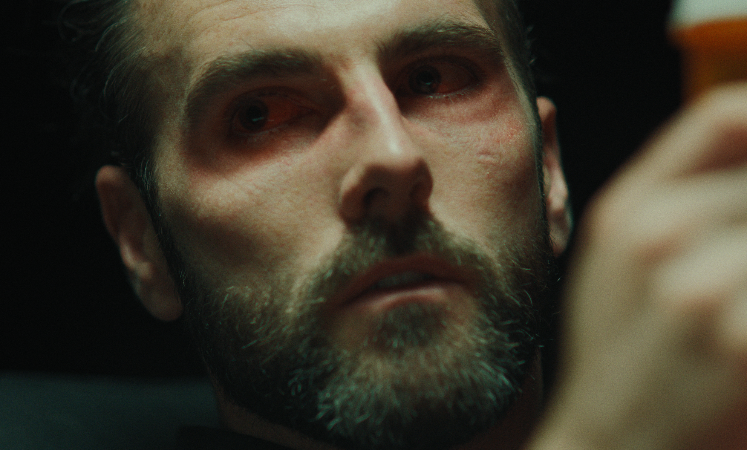 Close-up of a man with dark hair and beard, looking upward with a serious expression.