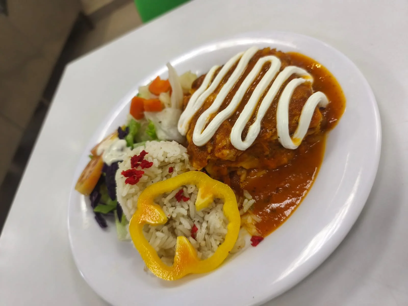 Plato de comida con arroz, ensalada, pollo con salsa y crema, y decoraciones de pimiento amarillo y rojo.