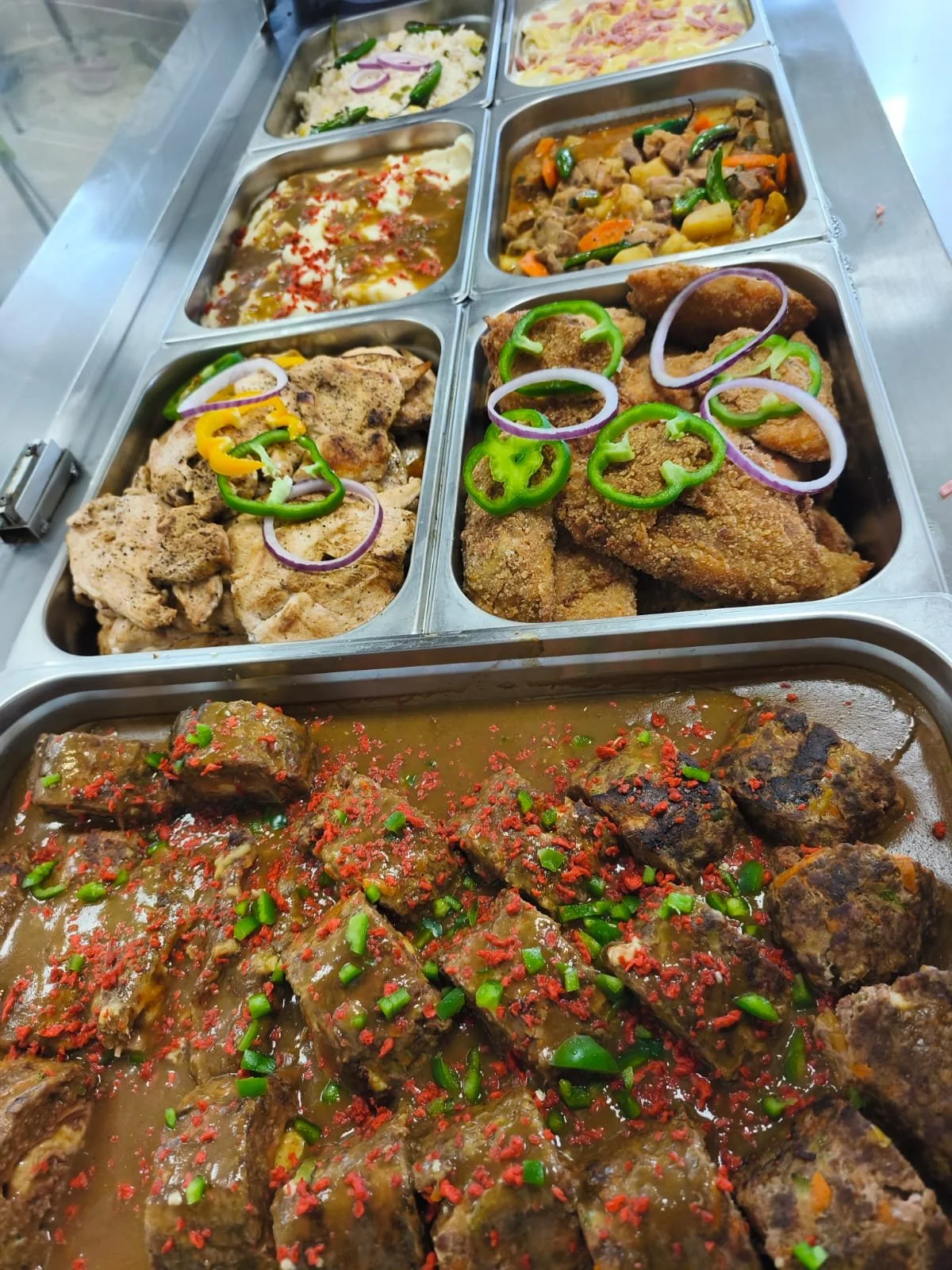 Variedad de platos tradicionales mexicanos en un buffet, incluyendo carne con salsas, pollo en trozos con cebolla y pimientos, guisos con verduras, y tacos en una bandeja.