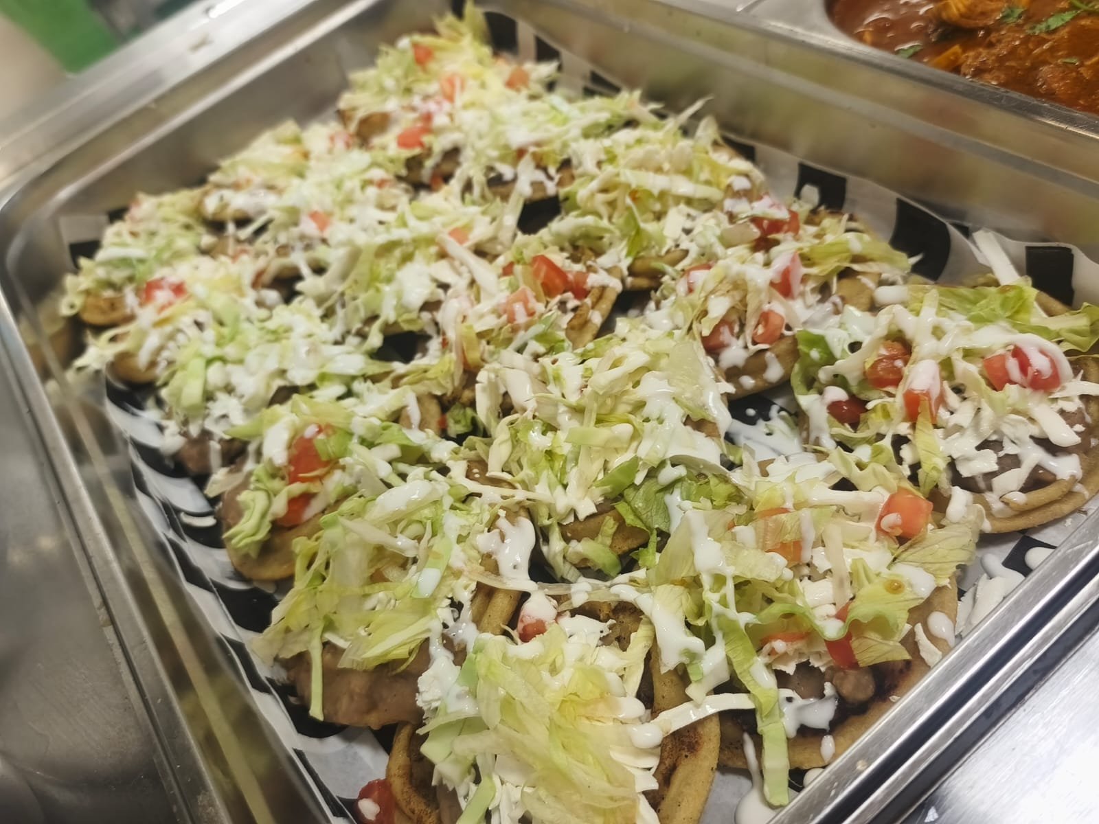 Tacos con carne, lechuga, jitomate y salsa en un plato metálico.