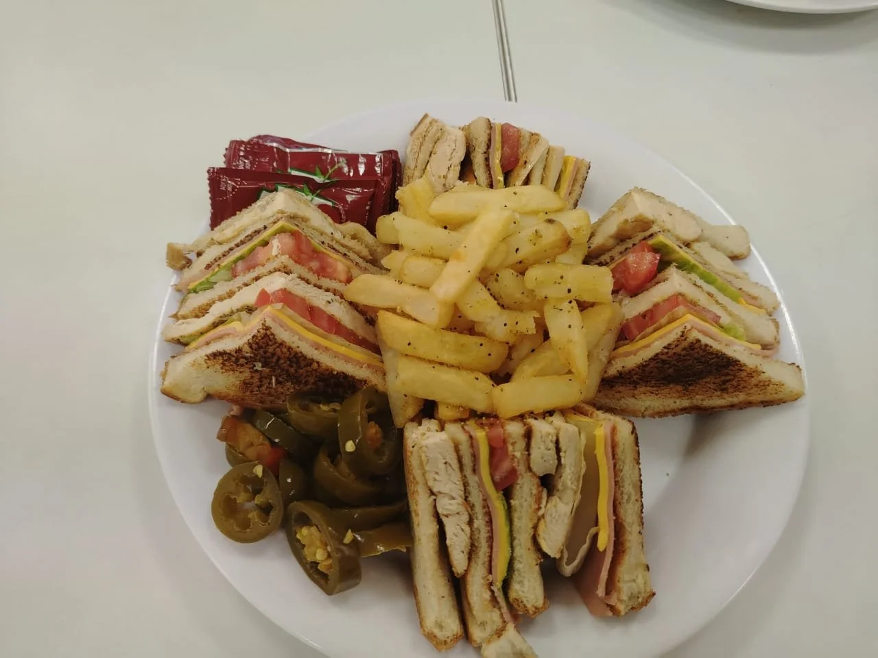 Plato con sándwiches cortados en triángulos, papas fritas, jalapeños en rodajas, y aderezo en sobre