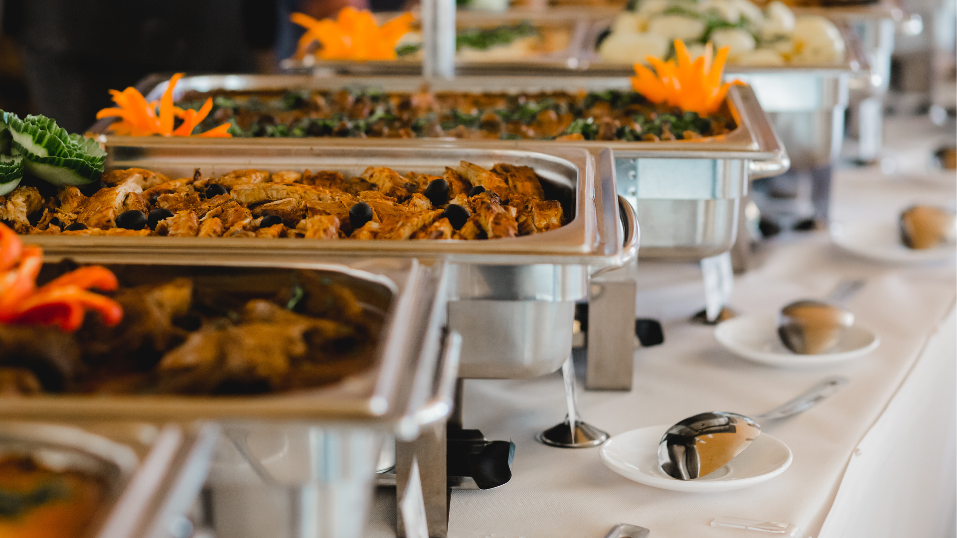 Variedad de platos de buffet con comida caliente y decoraciones con flores de colores en un evento.