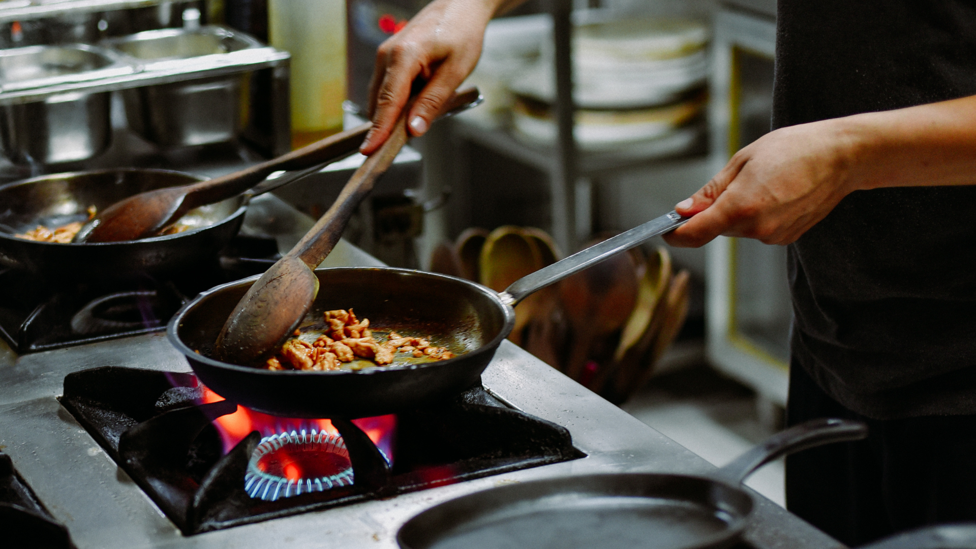 Persona cocinando con una sartén en una estufa a gas, removiendo alimentos cocidos.