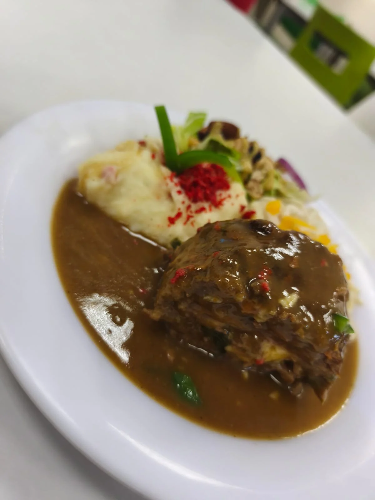 Plato con carne en salsa, puré de papas con trozos de tocino, y ensalada con vegetales variados.