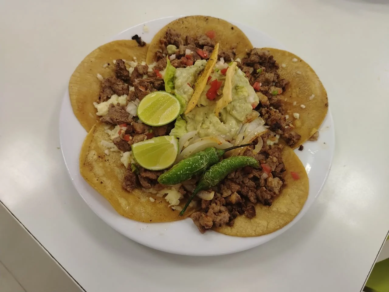Plato de tacos con carne, limones, chiles jalapeños, y guacamole.