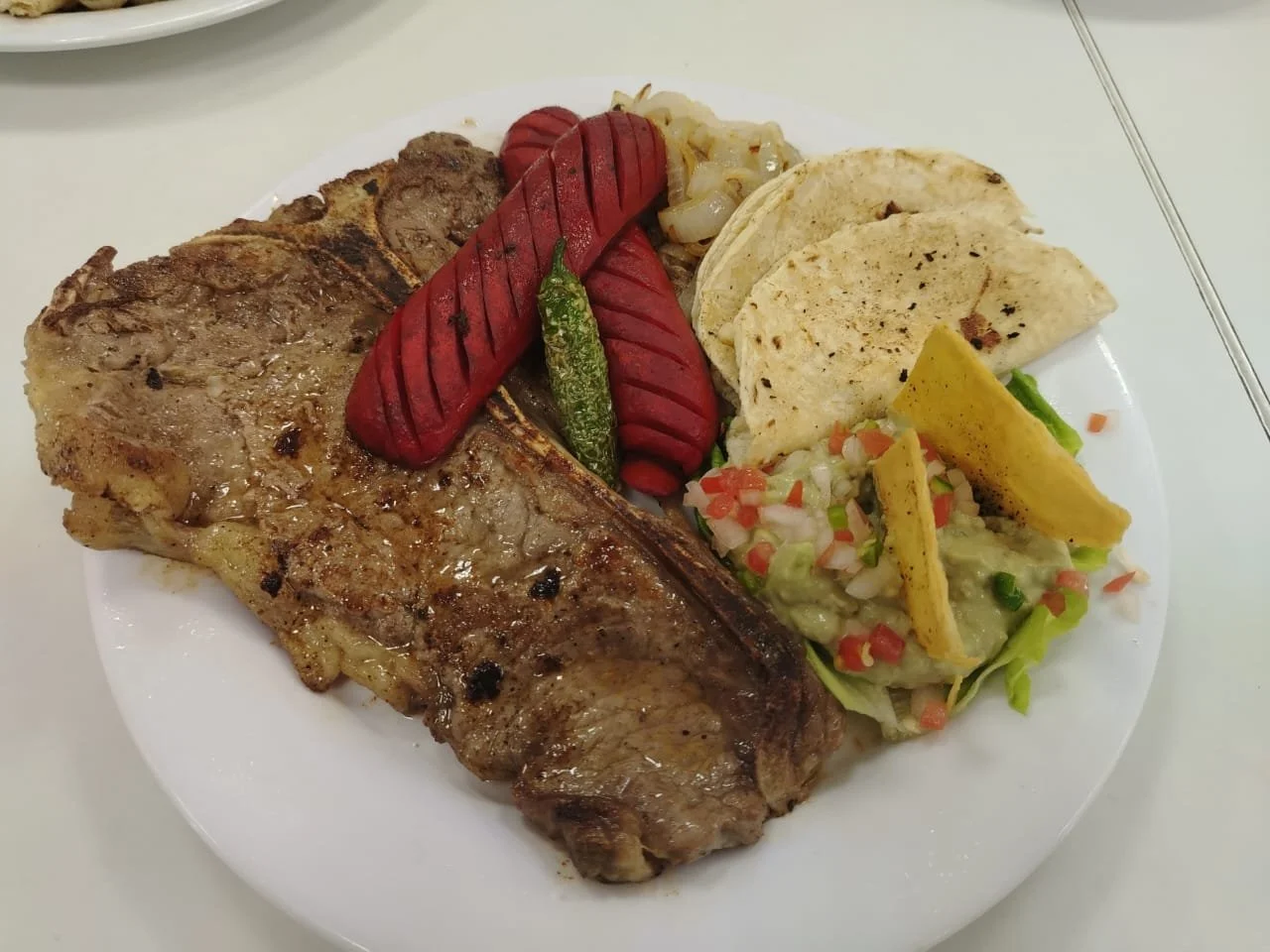 Plato con varios cortes de carne, chorizo, tortillas, guacamole con totopos, cebolla y salsa