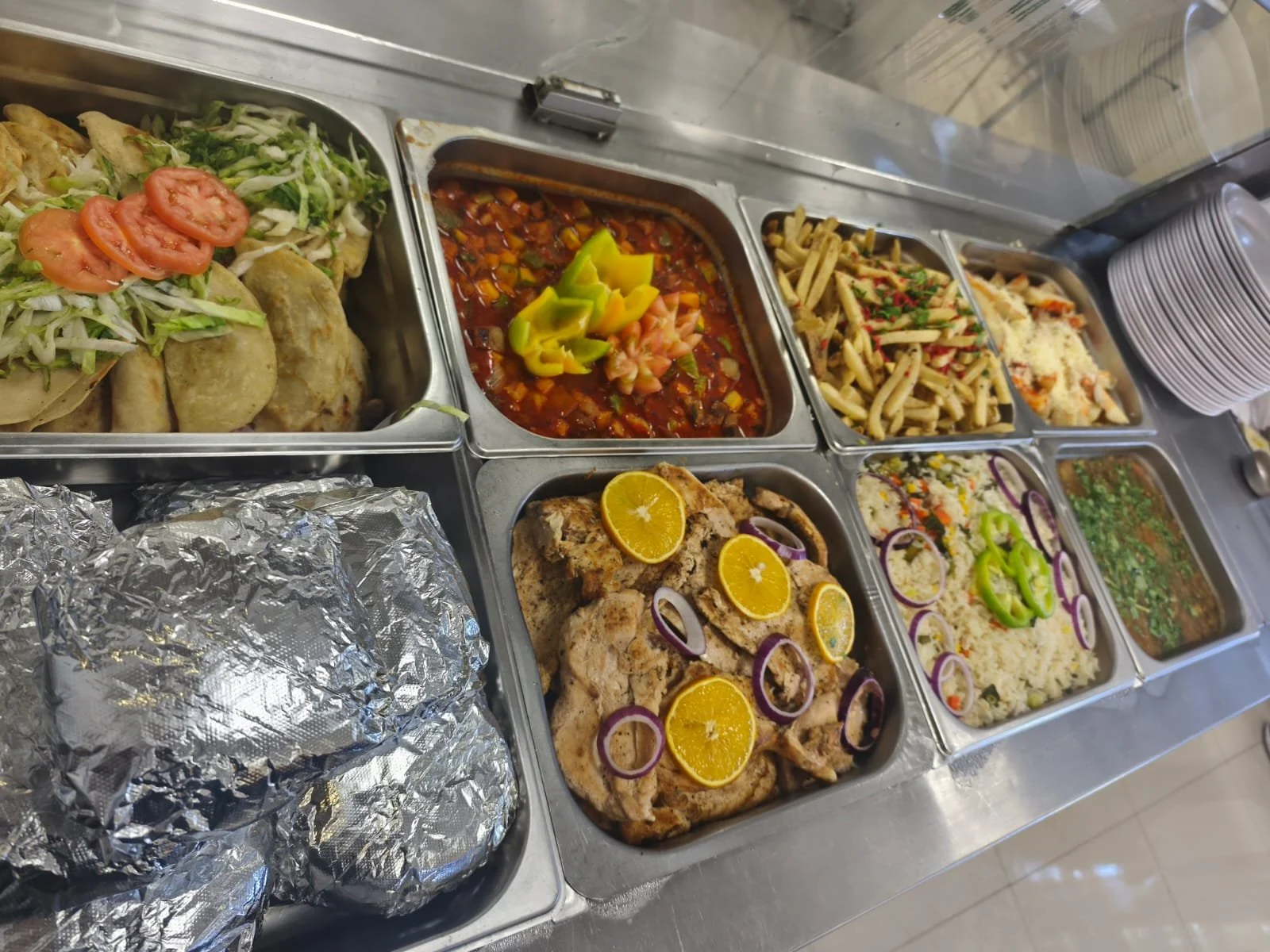 Variedad de platos de comida en un bufé, incluyendo tacos, ensalada, guiso de carne, pasta, pollo con limón, y arroz con verduras.