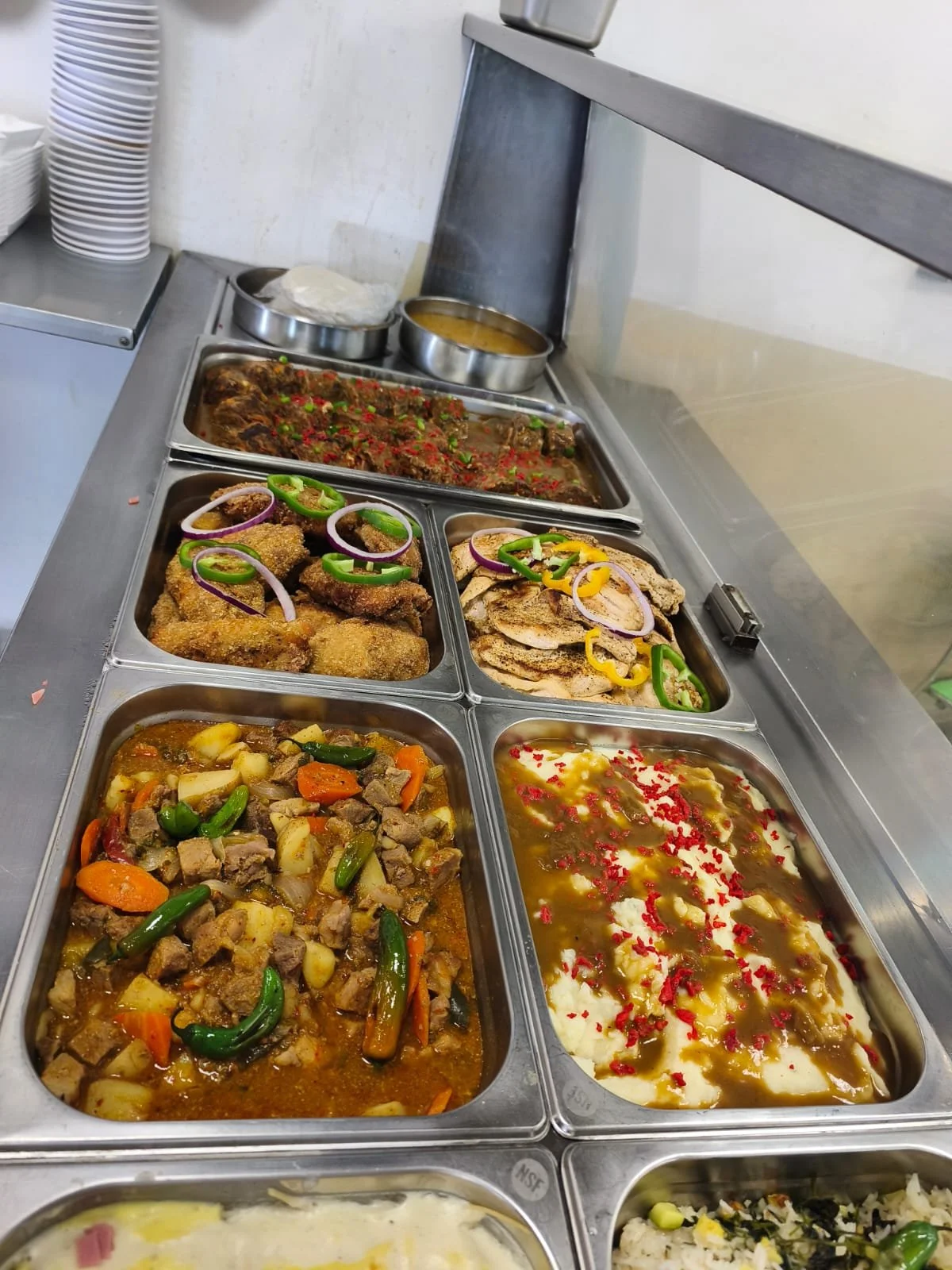 Variedad de platos típicos mexicanos en un bufé, incluyendo guisos con carne y verduras, frijoles, crema con red bits, y carnes con verduras.