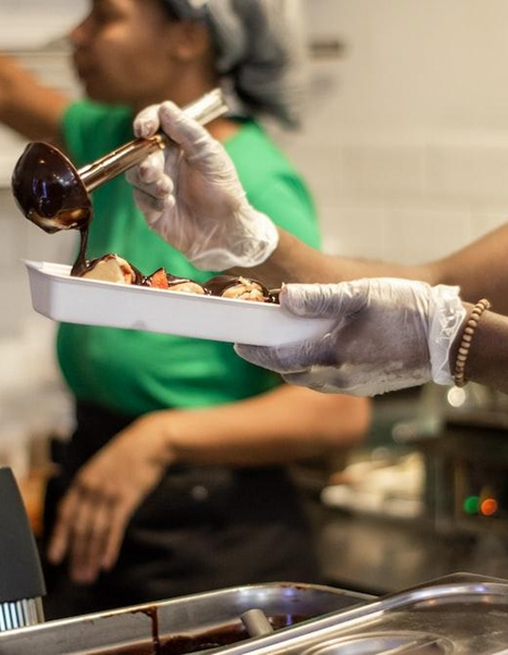 Persona sirviendo ganache de chocolate sobre un postre en una cocina.