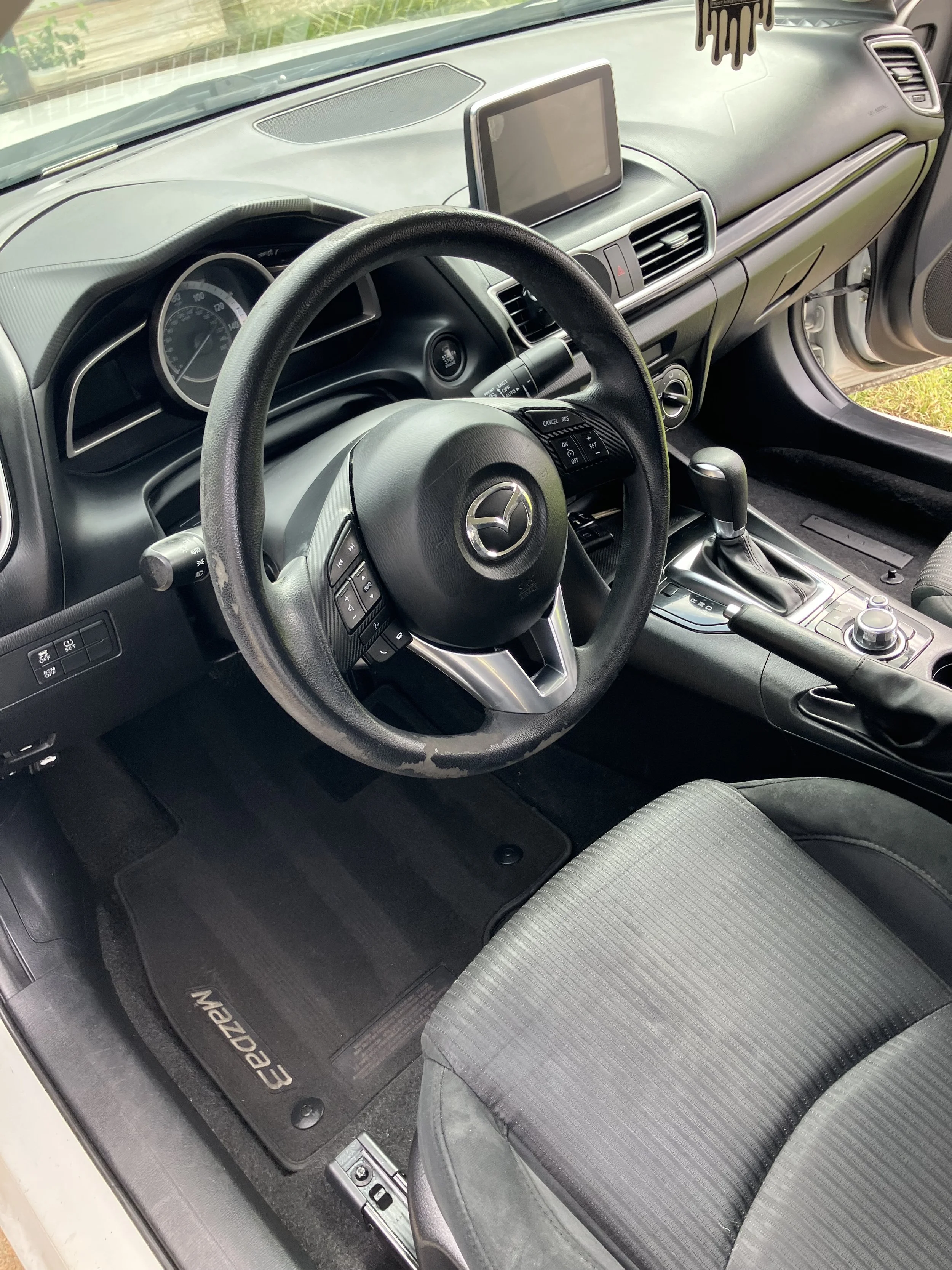 The interior of a Mazda CX-3 vehicle showing the steering wheel, dashboard, gear shift, and front passenger seat.