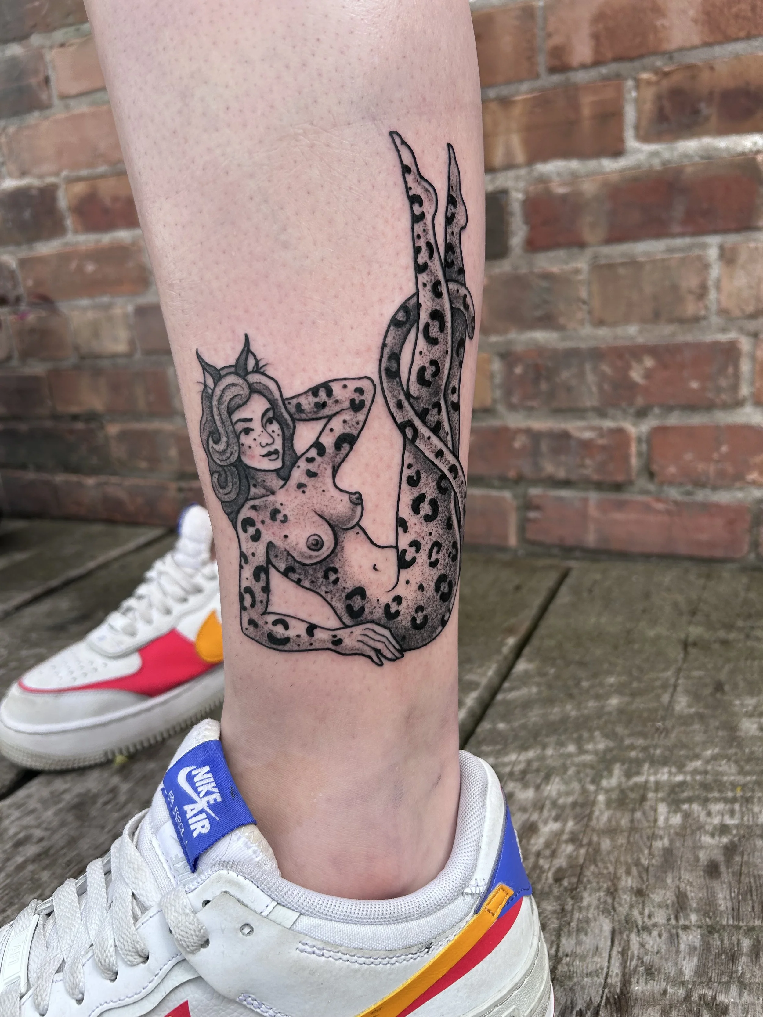 Tattoo of a leopard girl with cat ears and long hair, stretching with one leg in the air, on a person's calf.