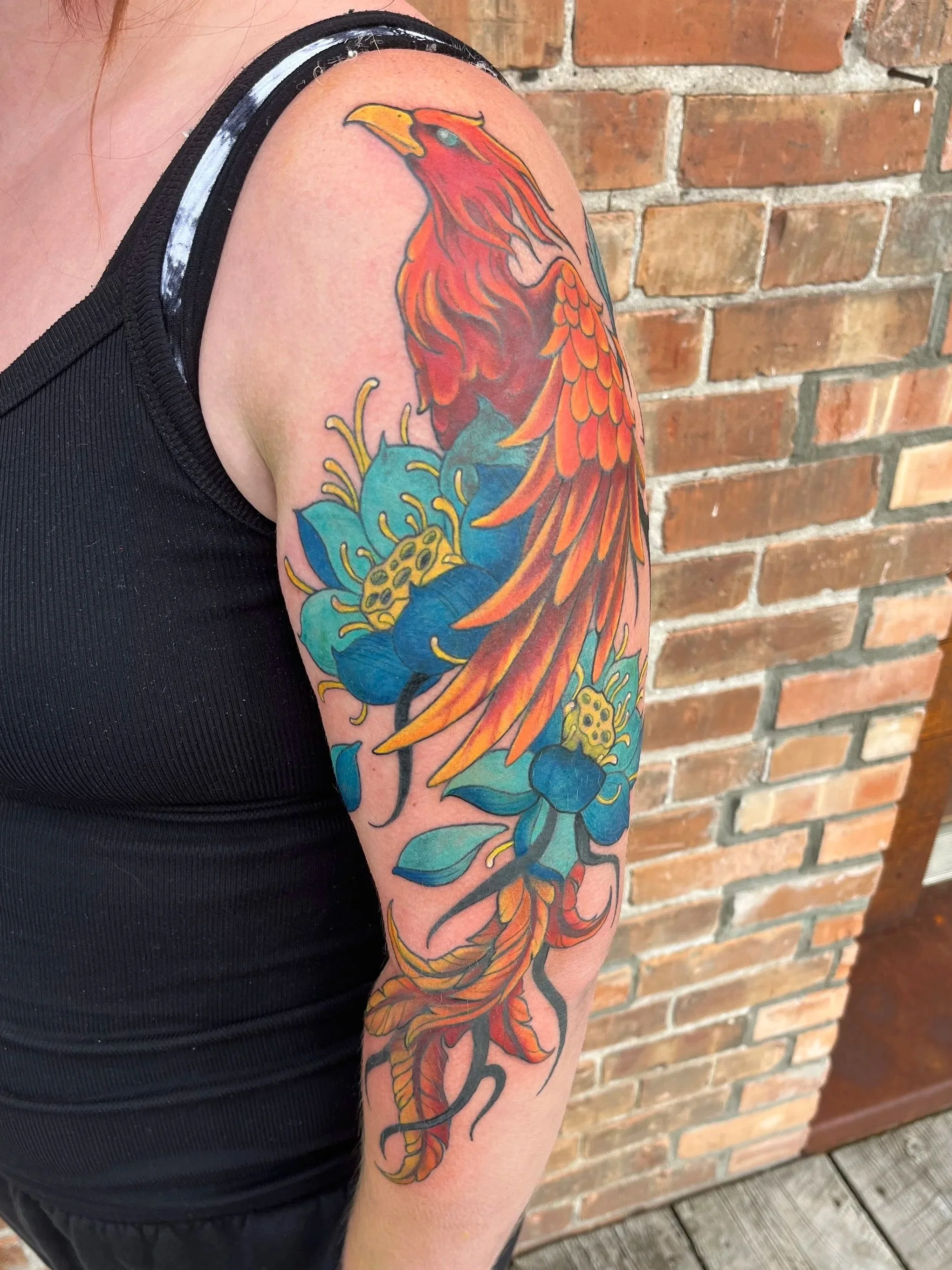 Colorful tattoo of a phoenix on a person's upper arm.