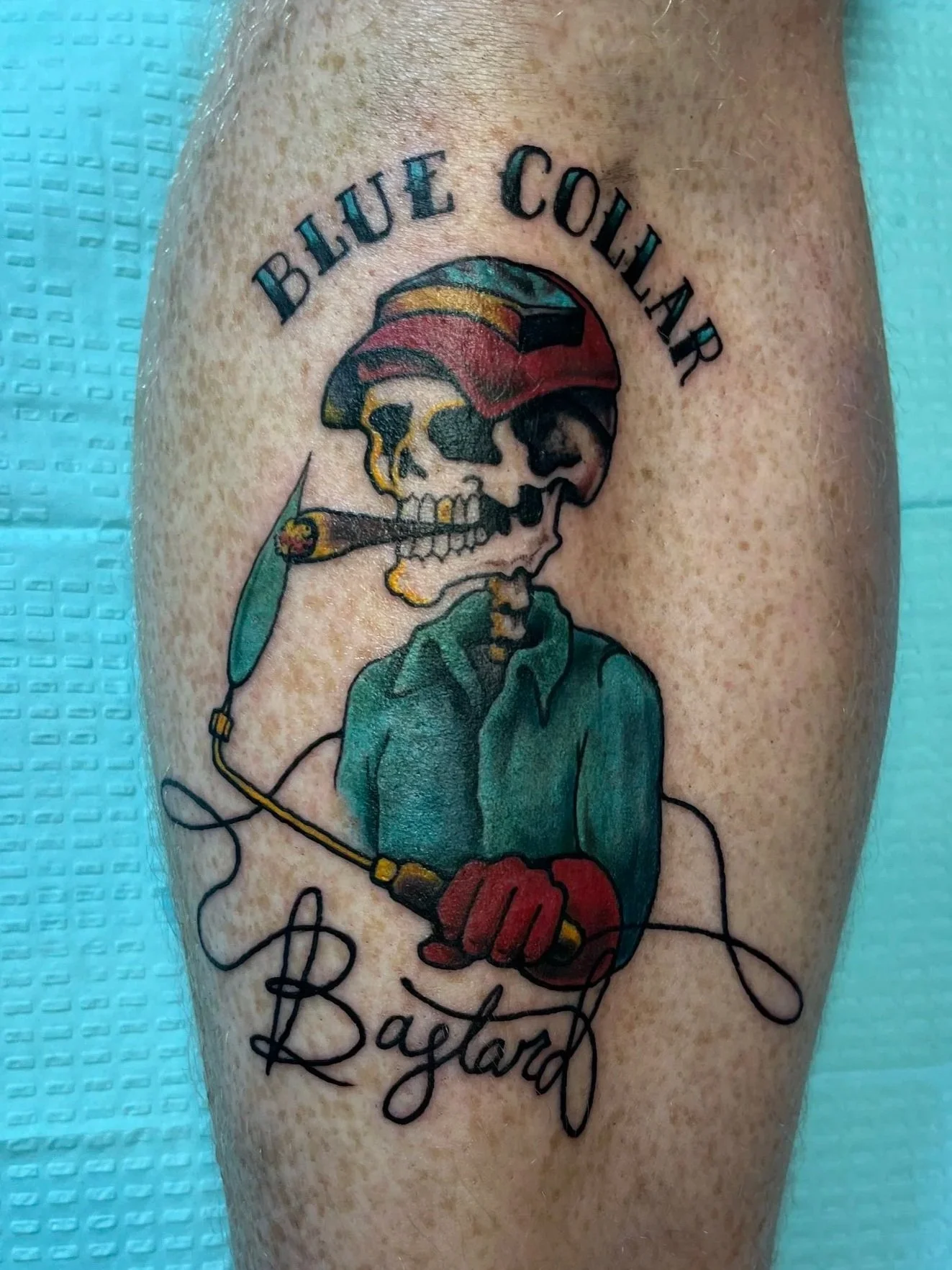 Tattoo of a skeleton with a helmet, smoking a cigar, holding a marlin, and wearing fishing gloves, with the word 'Baylor' written underneath.