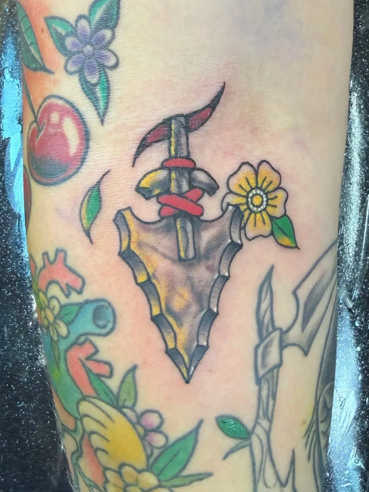 A tattoo of a dagger with a snake wrapped around it, flowers, and leaves.