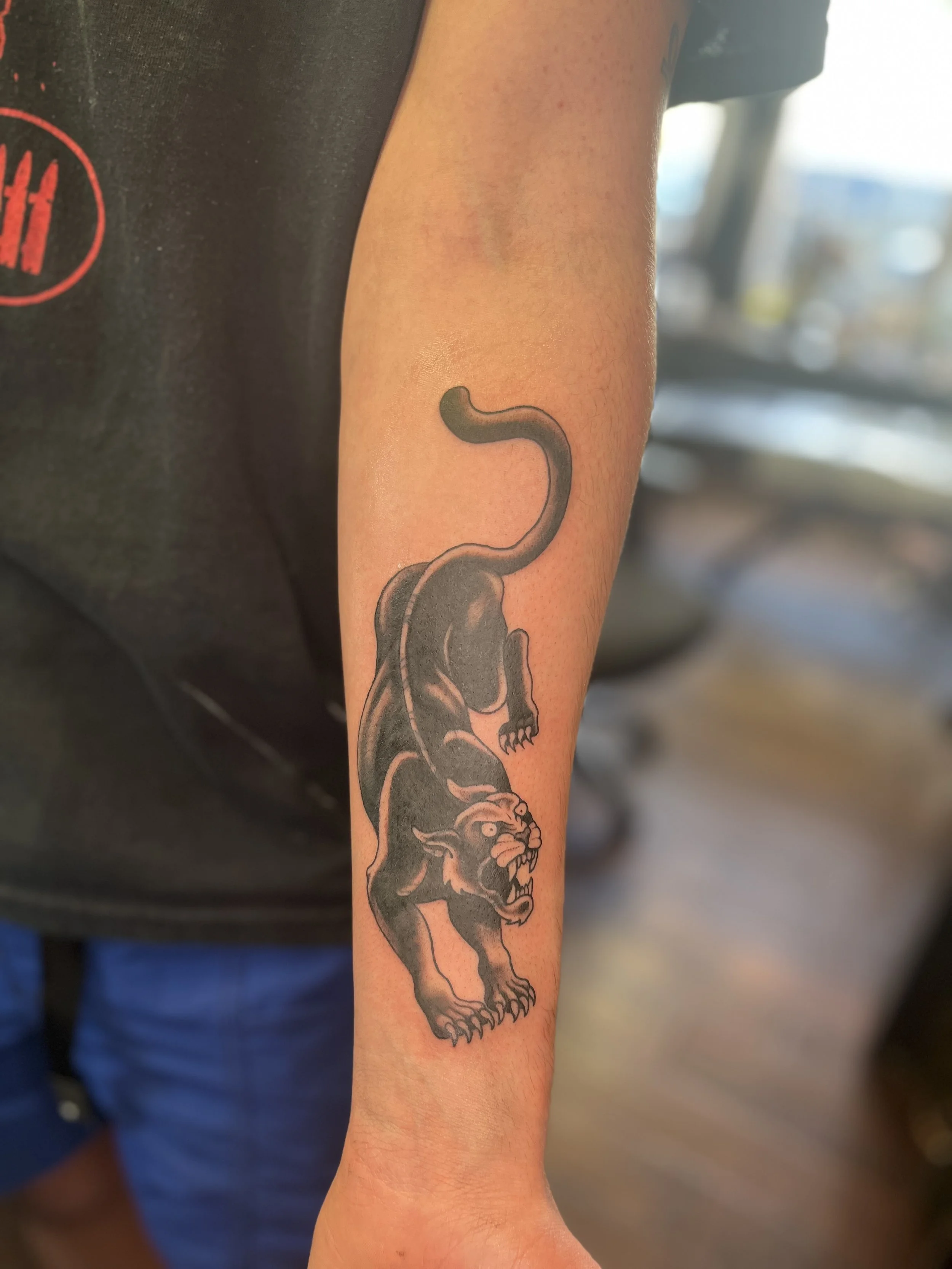 Tattoo of a fierce lion on a person's forearm, with a serpent originating from its mouth, in black ink.