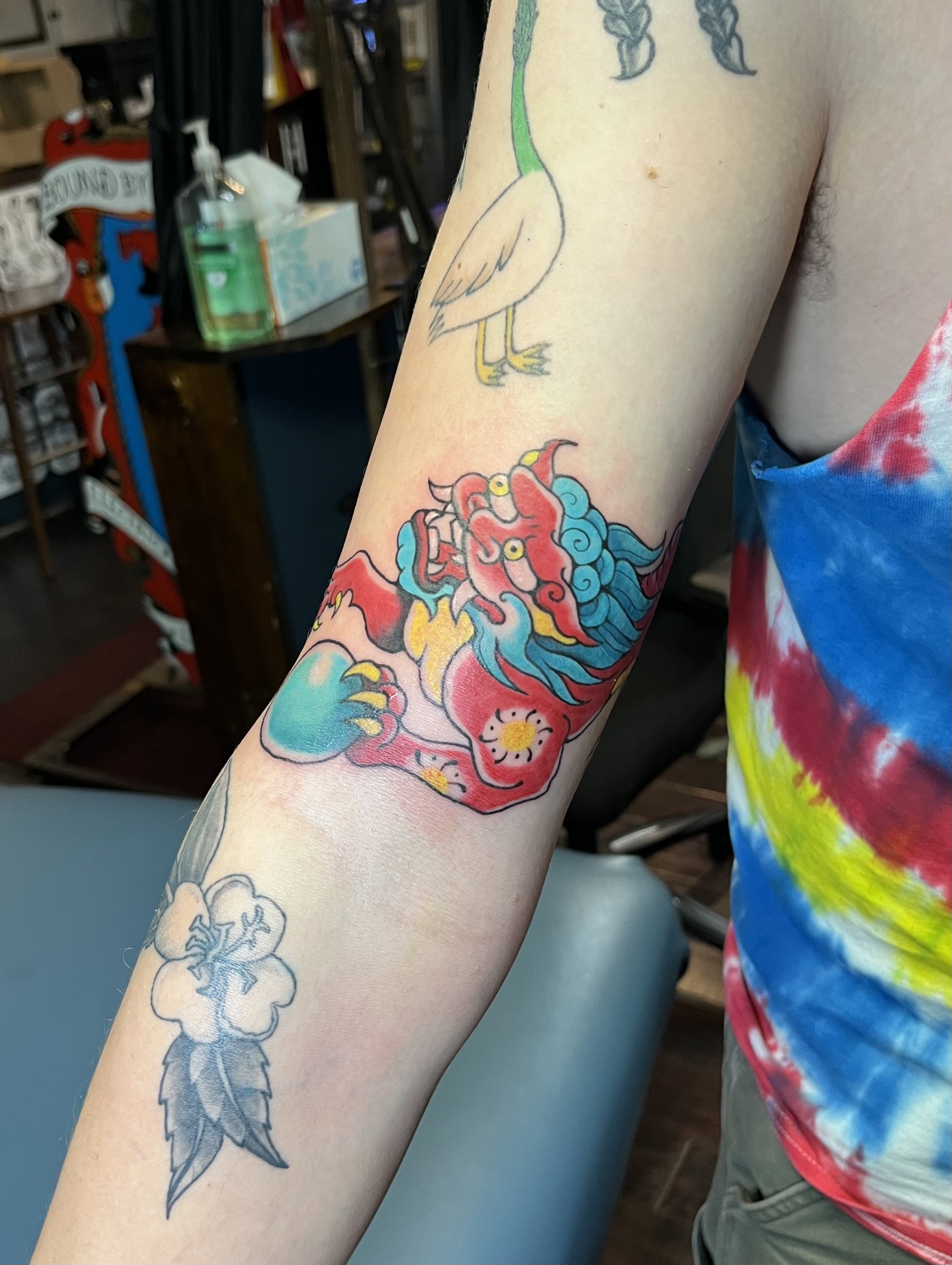 Close-up of a person's arm displaying colorful tattoos of a dragon, a bird, and a cloud motif.