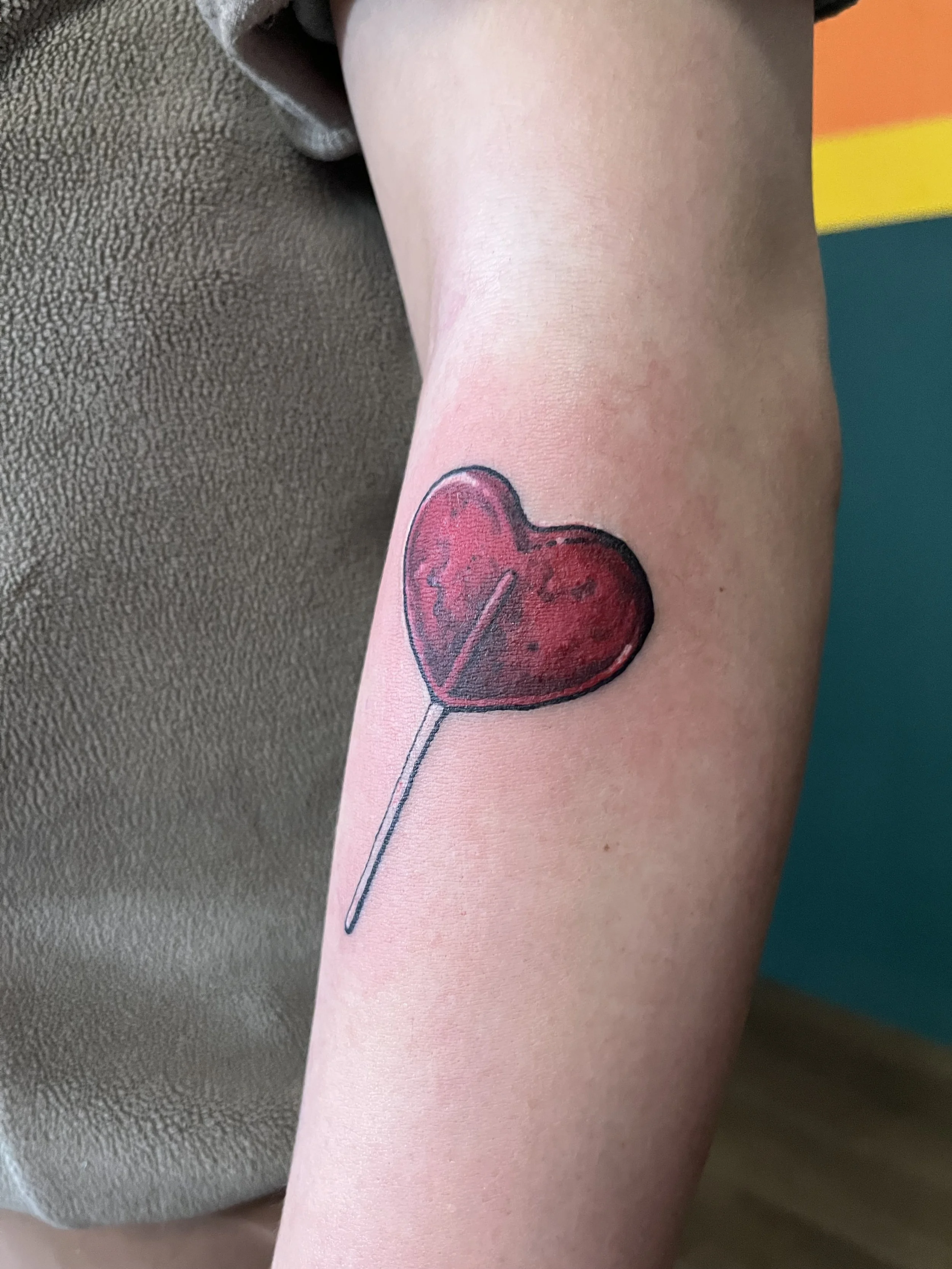 A tattoo of a red heart with a heartbeat line on a person's upper arm.