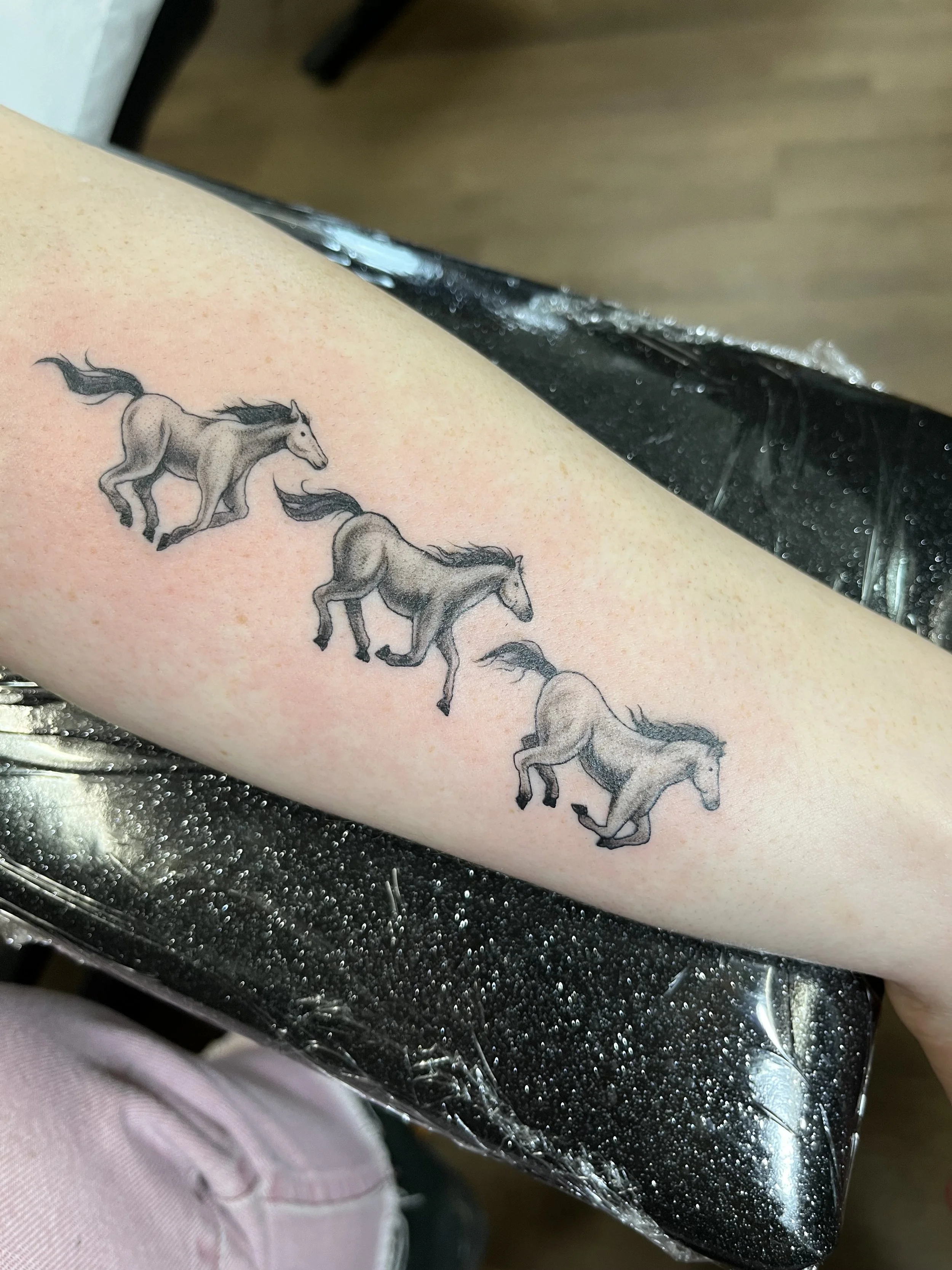 Tattoo of gray horses in a row on a person's skin.