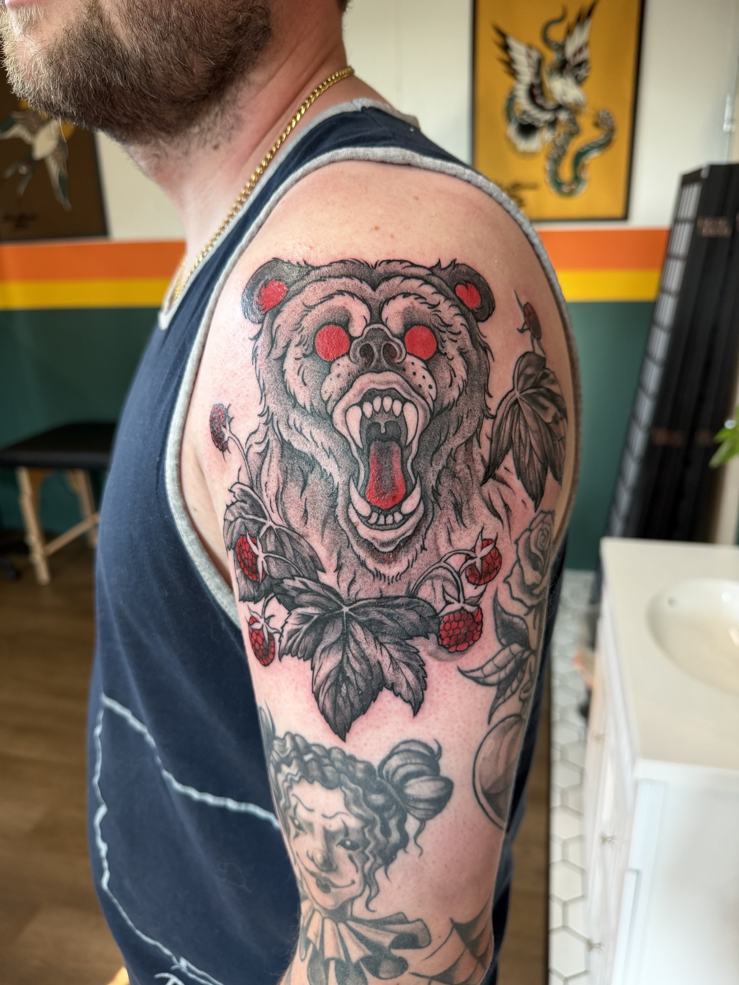 Tattoo of a roaring bear with red eyes and berries on its claws, on a man's upper arm.