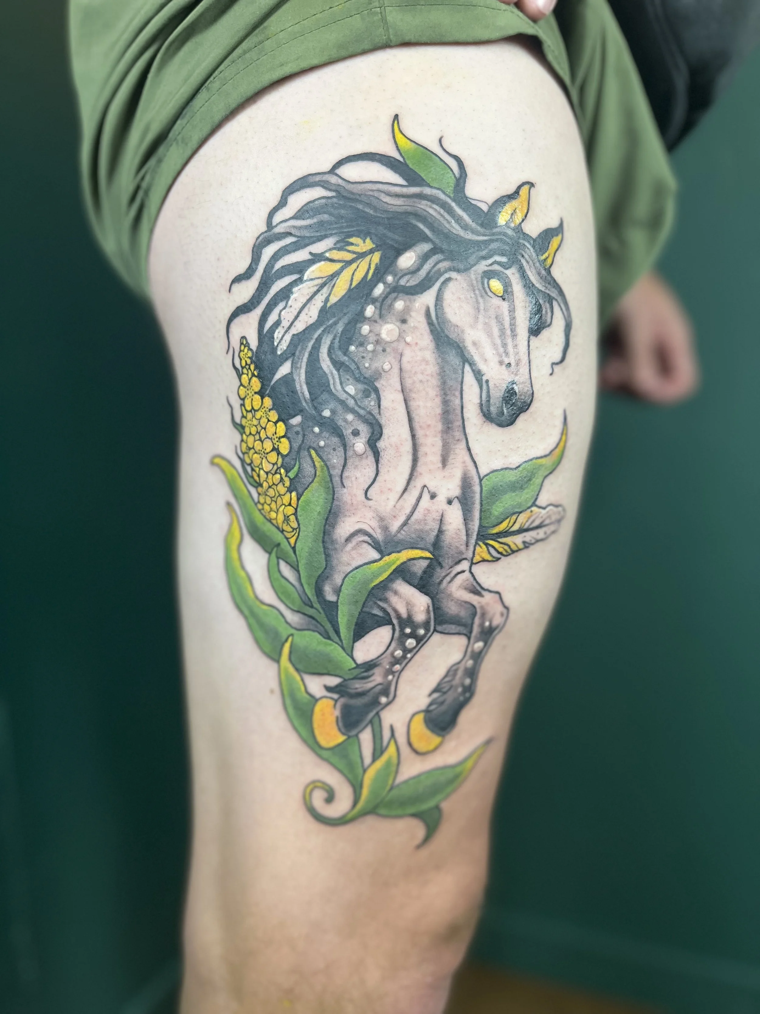 A colorful tattoo of a horse with a flowing mane and yellow leaves on the shoulder and upper arm.
