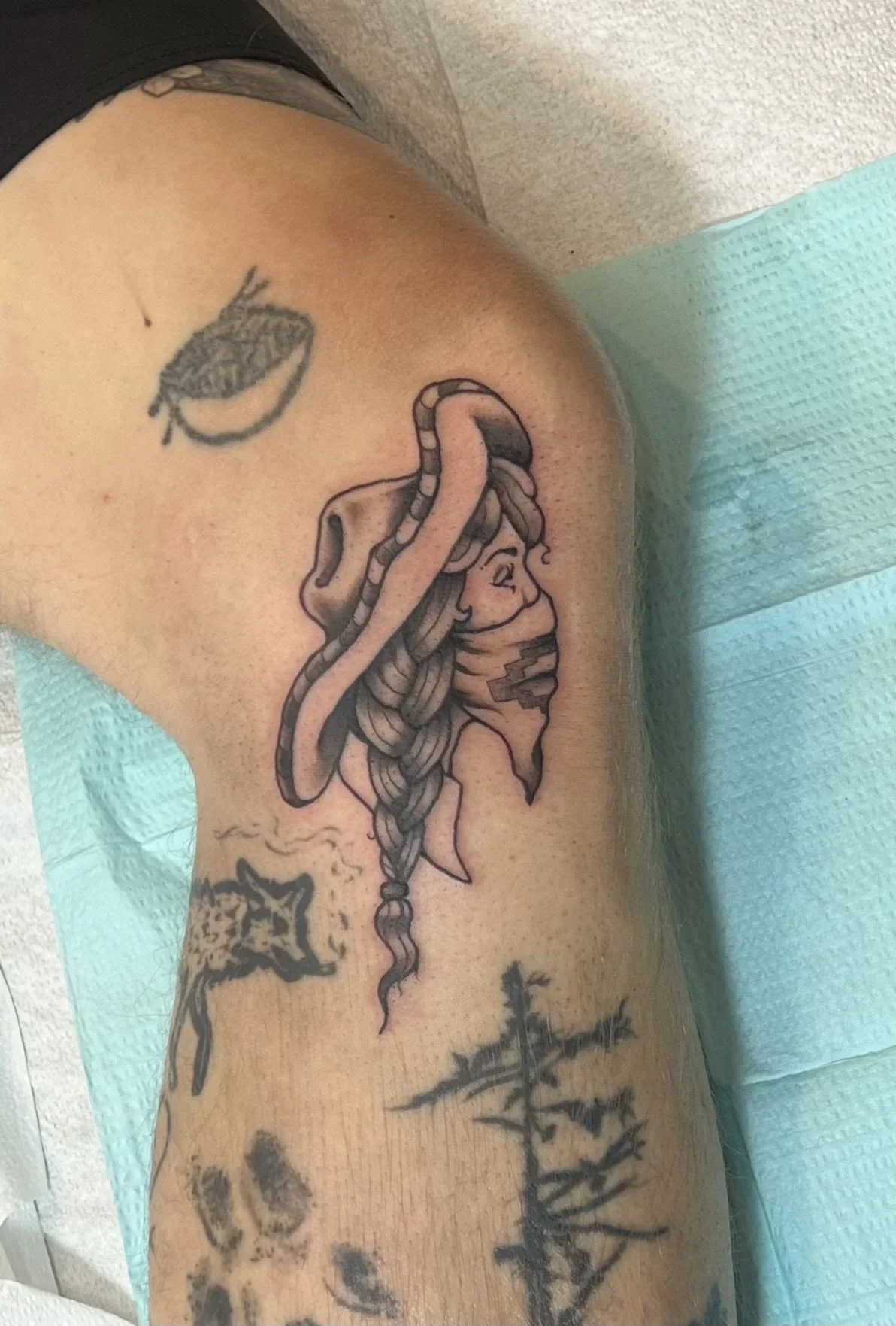 A tattoo of a woman's face with long braided hair and a snake wrapping around her head, located on a person's upper arm.