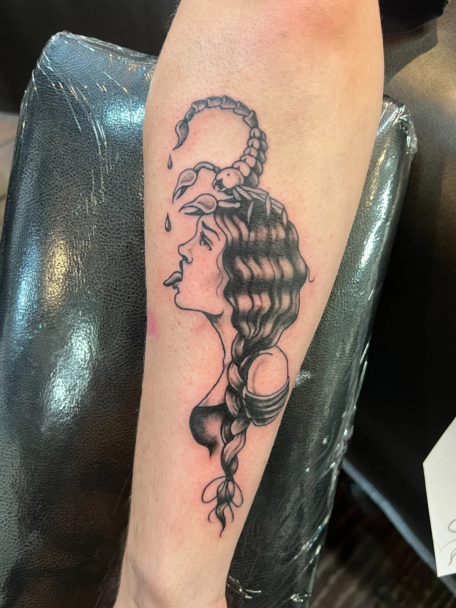 Tattoo of a human face with flowing hair, with a scorpion emerging from the top of the head. The scorpion appears to be dripping something from its claws.