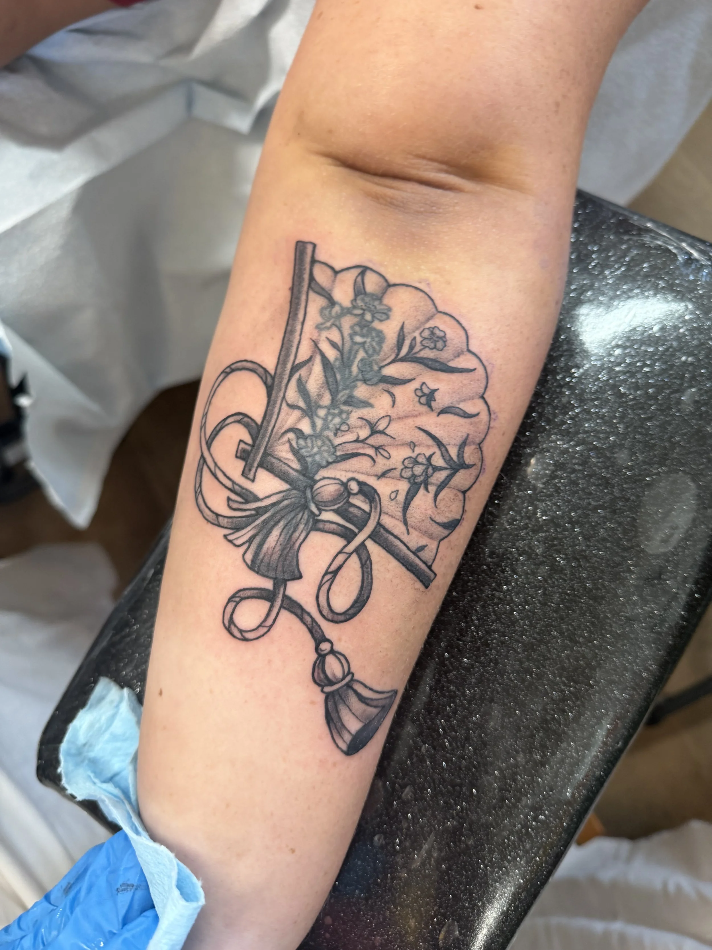 A tattoo of a key intertwined with floral and ribbon designs on a person's forearm.