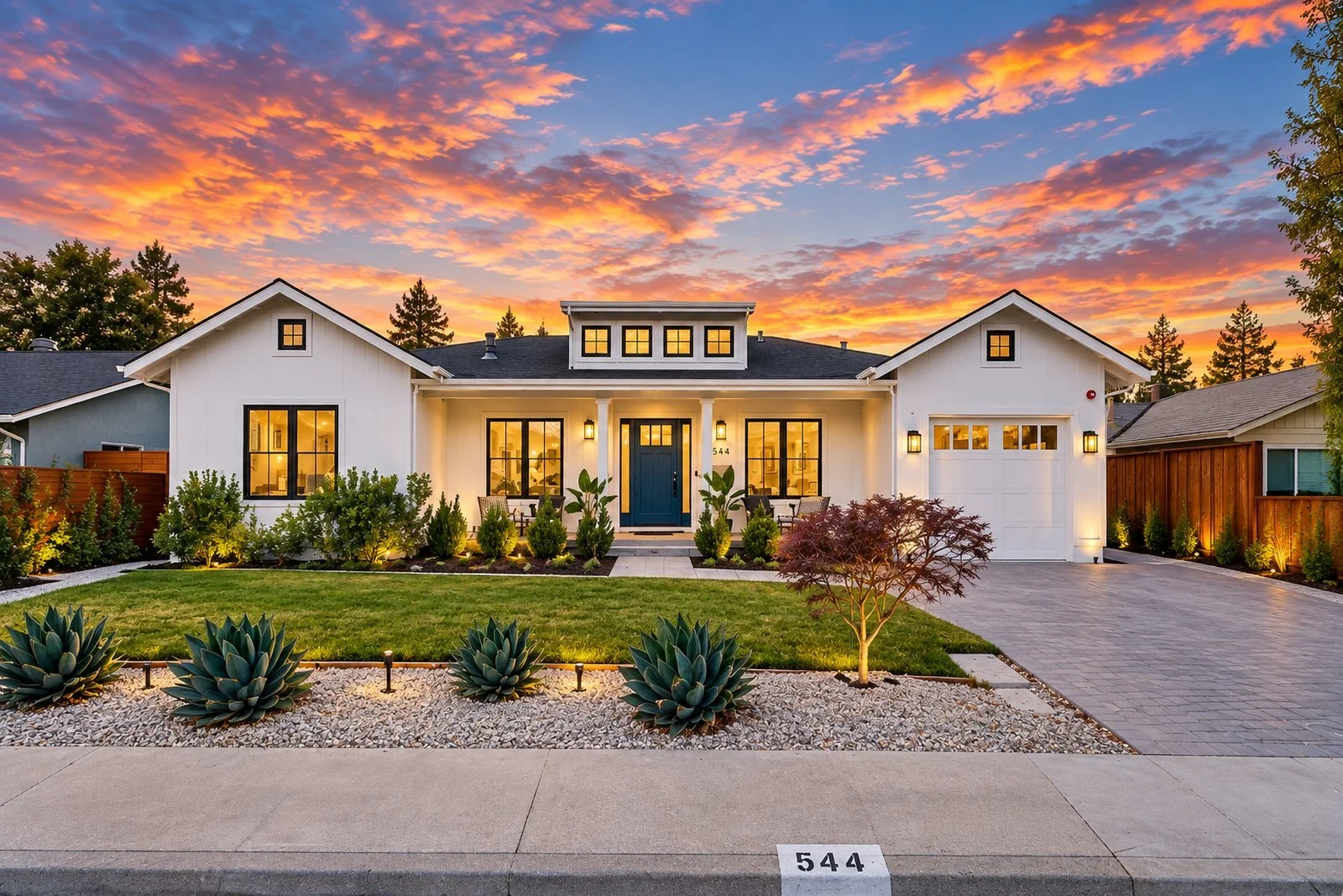 White modern farmhouse with a landscaped front yard at sunset