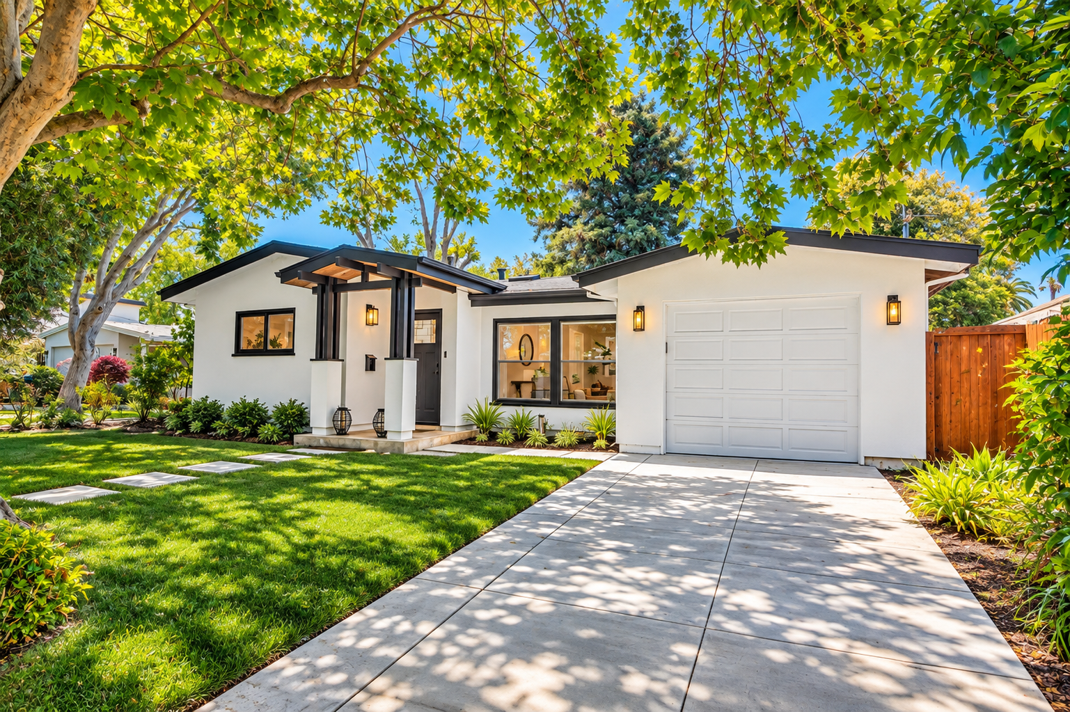A modern white house with black accents, a single-car garage, and a lush green front yard with trees and plants, under a clear blue sky.