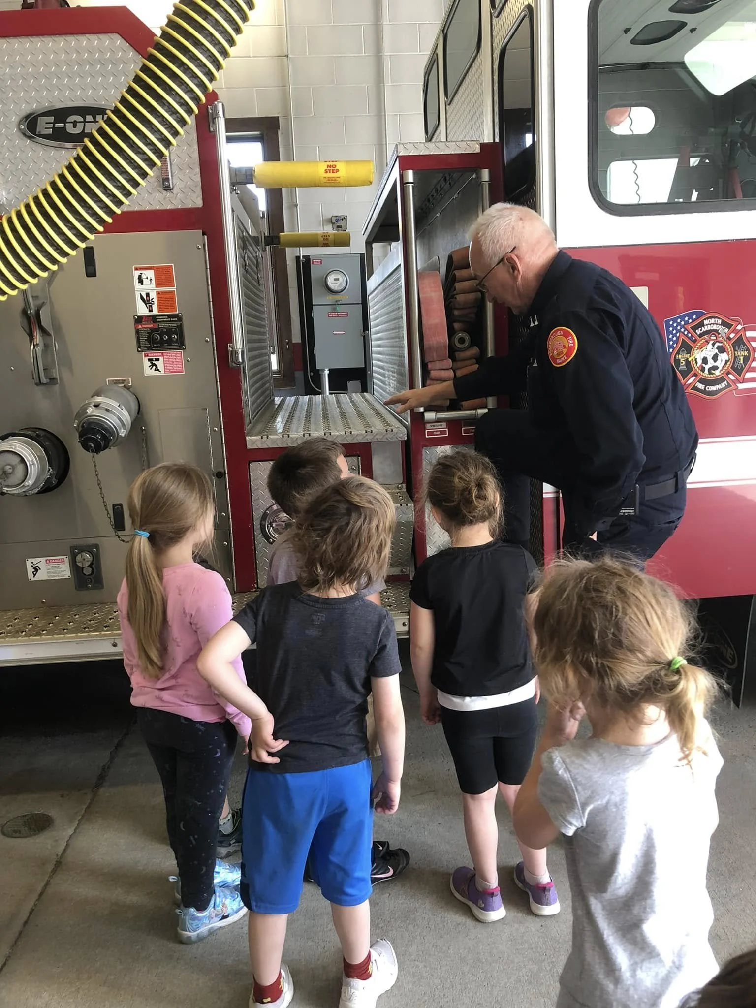 A firefighter showing a group of children the inside of a fire truck.