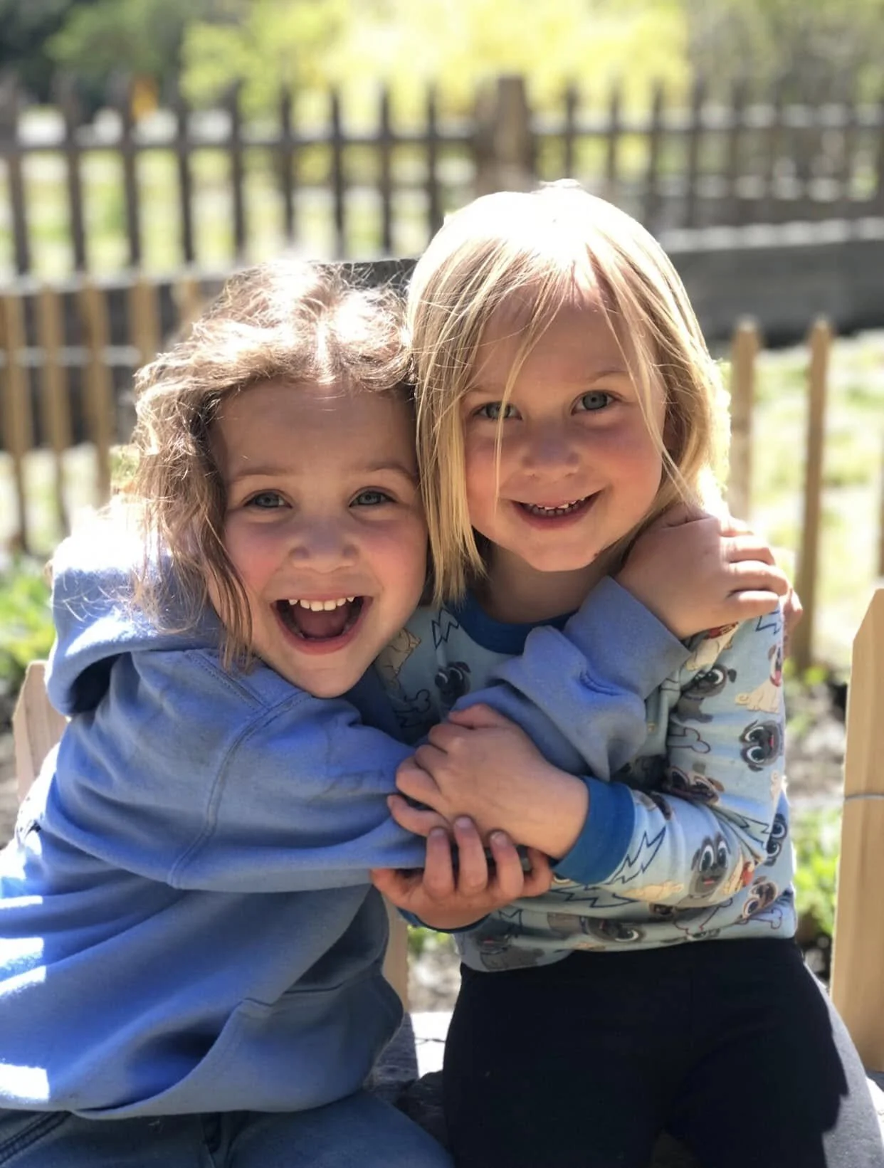 Two children, a girl and a boy, smiling and embracing outdoors on a sunny day.