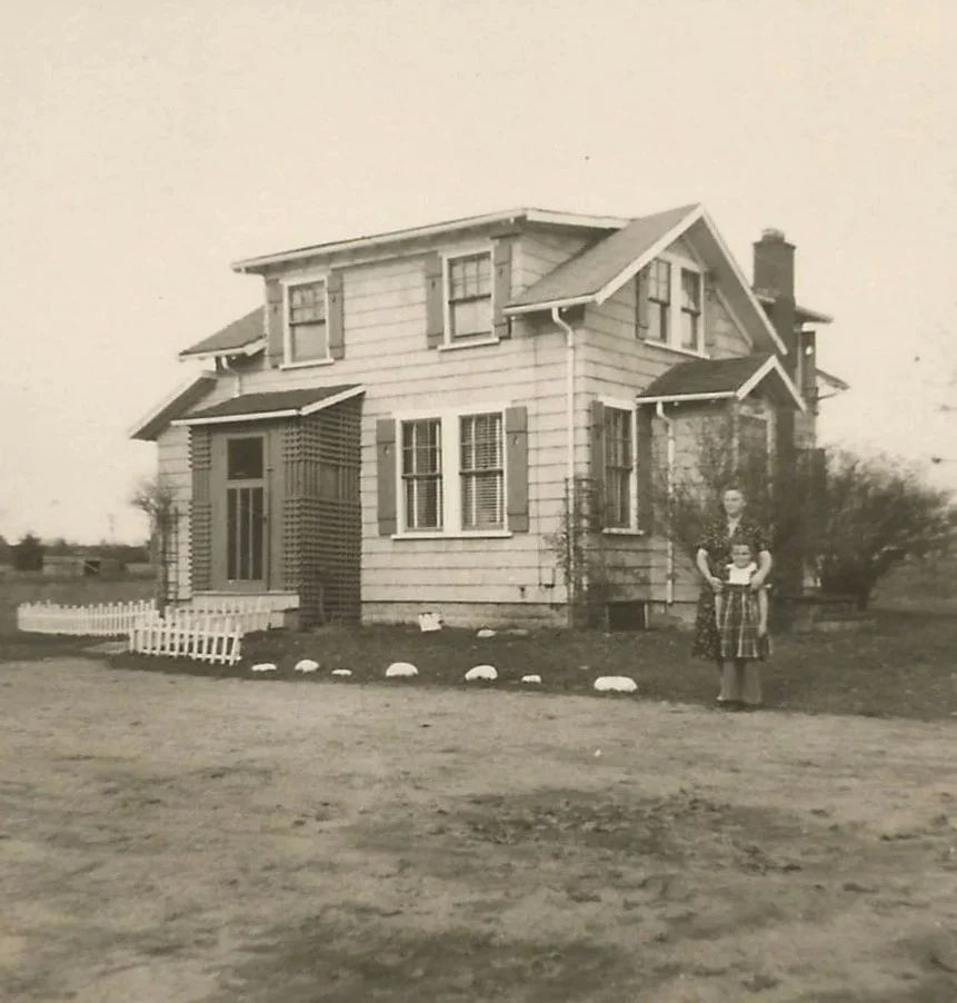 A vintage black-and-white photo of a woman and a girl standing in front of a two-story house with clapboard siding, surrounded by a small white picket fence and a dirt yard at 4 Saco Street, Scarborough, Maine. Now the location of Soreil Farm Store.