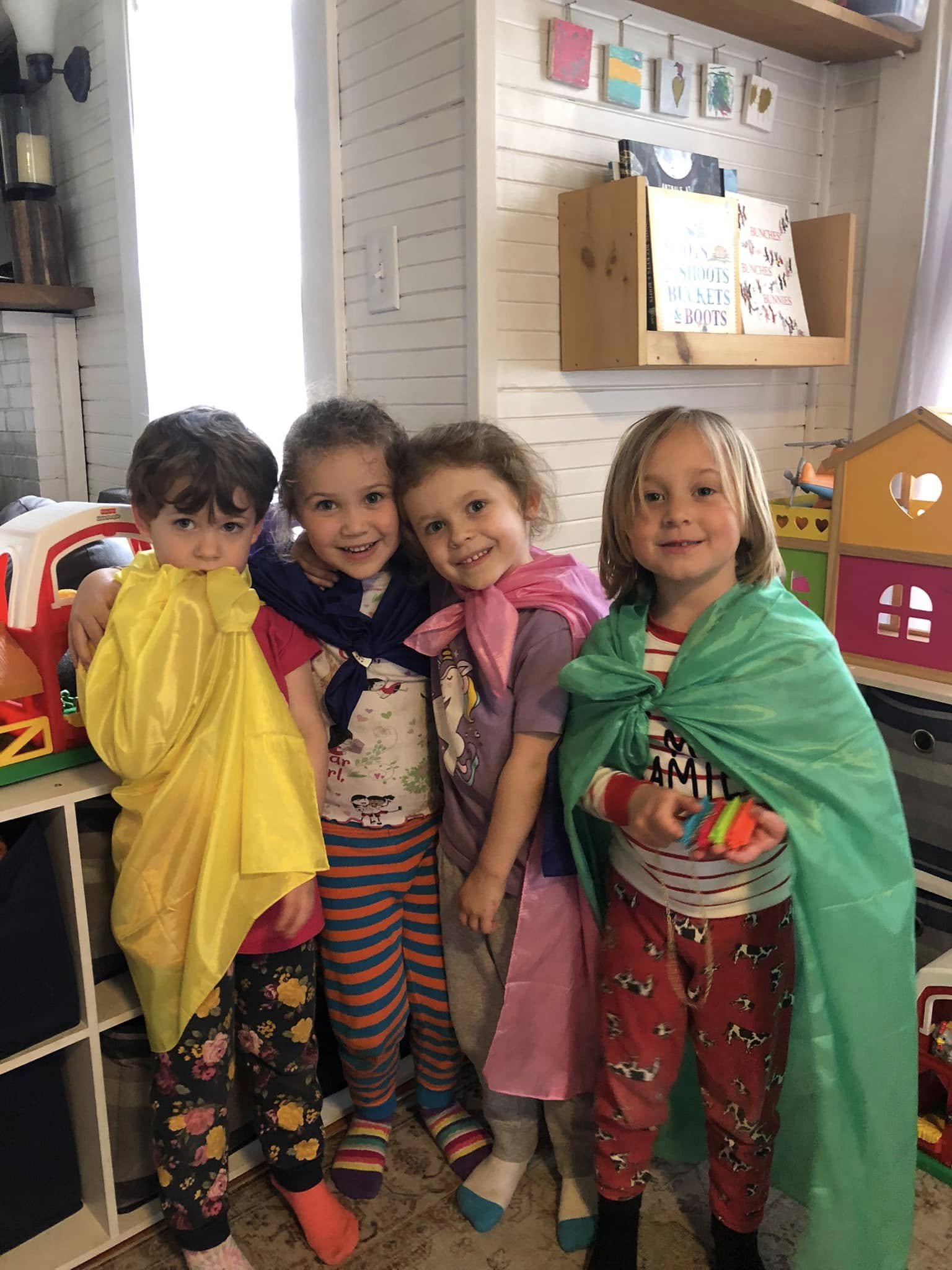 Four young children standing together indoors, dressed in colorful pajamas and robes, smiling and posing for a photo.