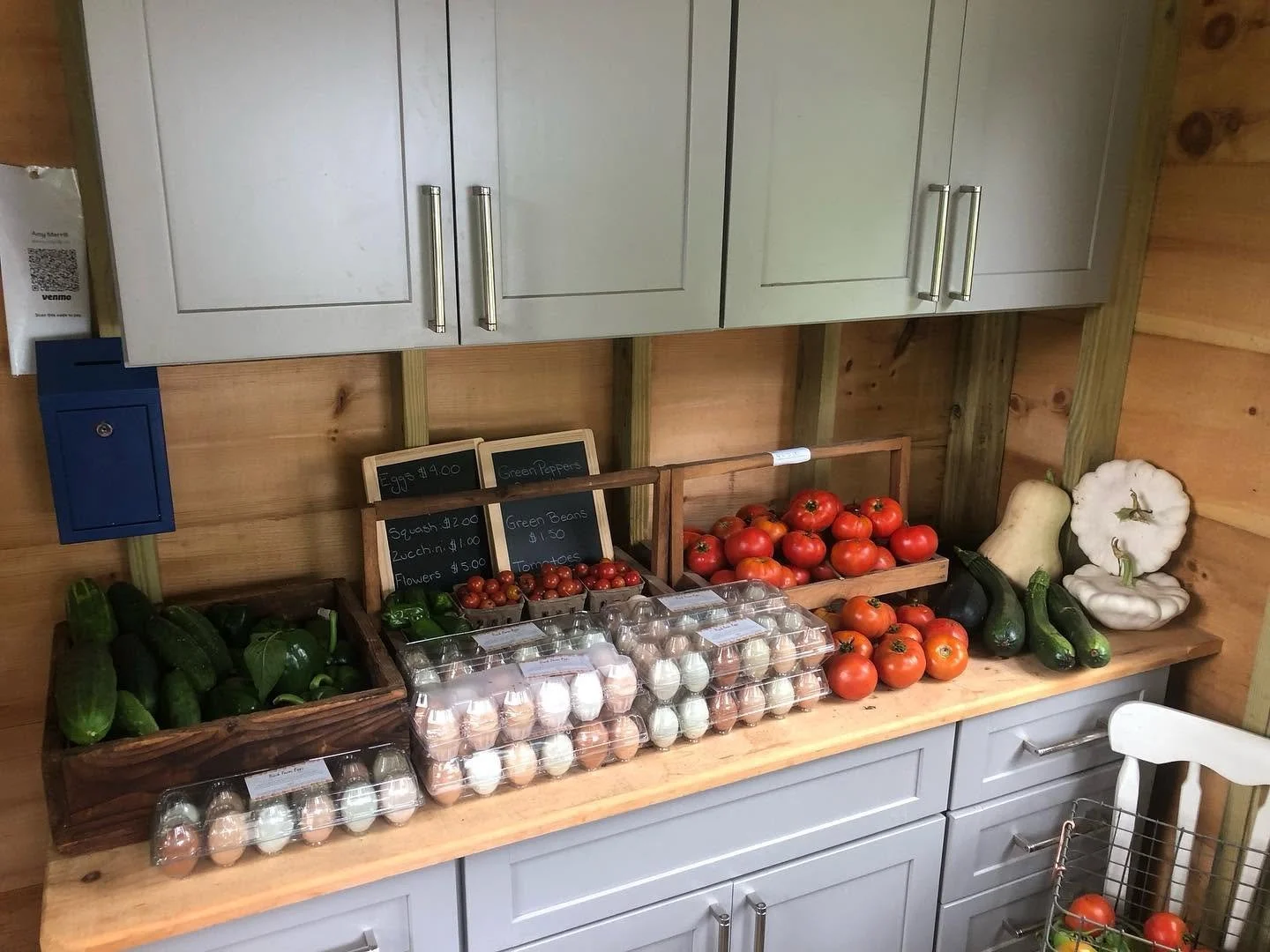 Fresh vegetables and eggs are displayed on a wooden counter in Soreil Farm store in Scarborough, Maine. Includes cucumbers, cherry tomatoes, larger tomatoes, white and green pumpkins, and eggs in plastic cartons.
