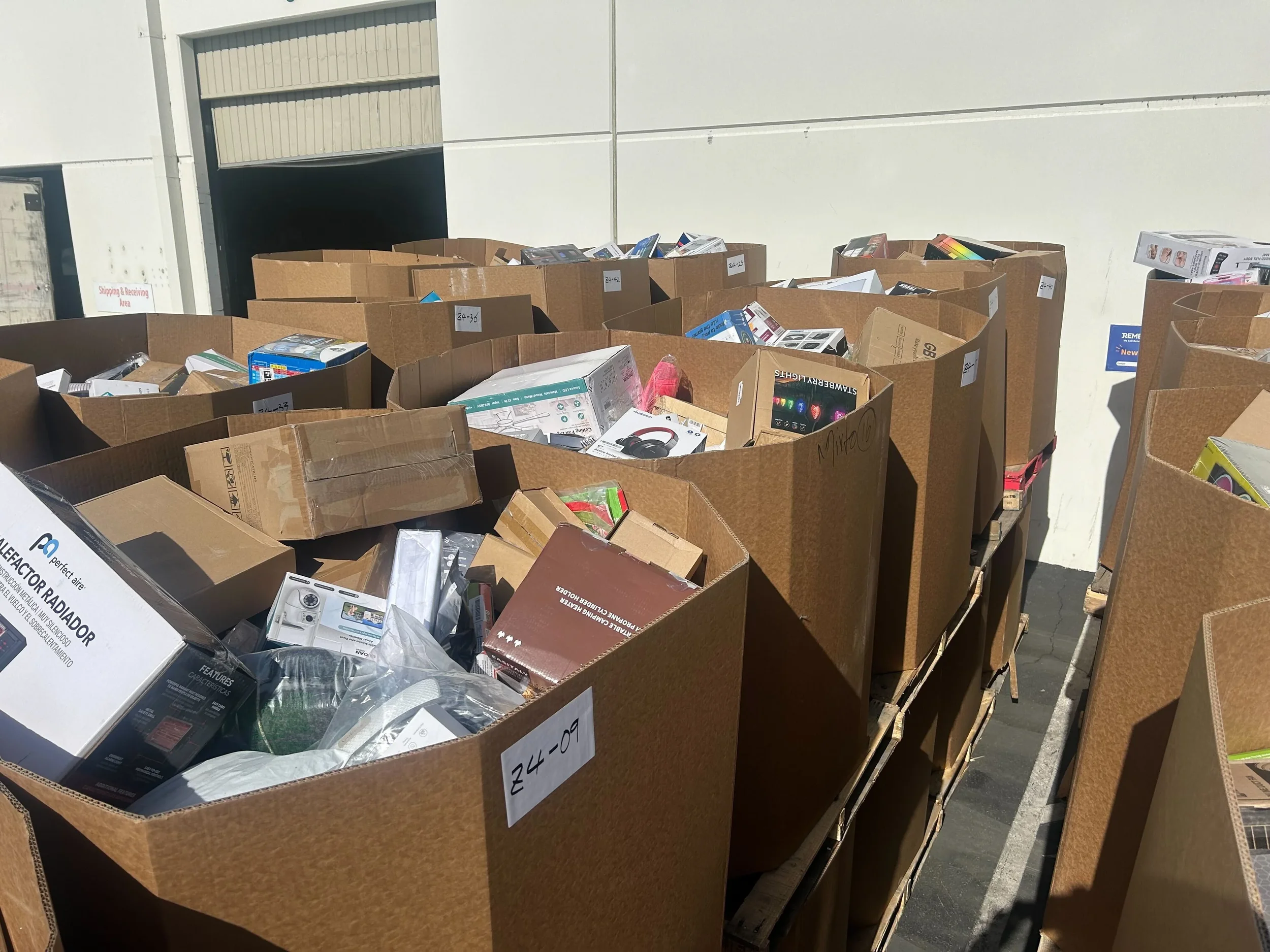 Multiple cardboard boxes filled with electronics and small appliances outside a warehouse near a loading door.