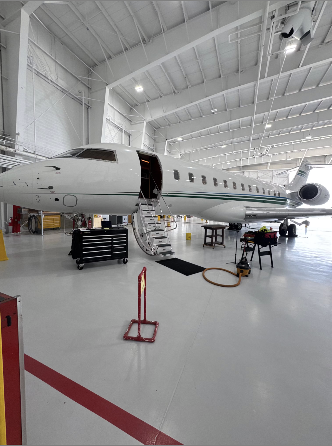 Commercial airplane inside the hangar, with open entry door, stairs leading into the aircraft, and maintenance equipment around.