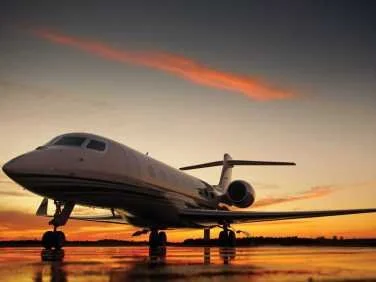 Private jet airplane parked on runway during sunset sky.