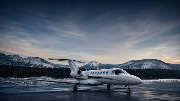 A private jet parked on a snowy runway with mountains in the background at dusk.